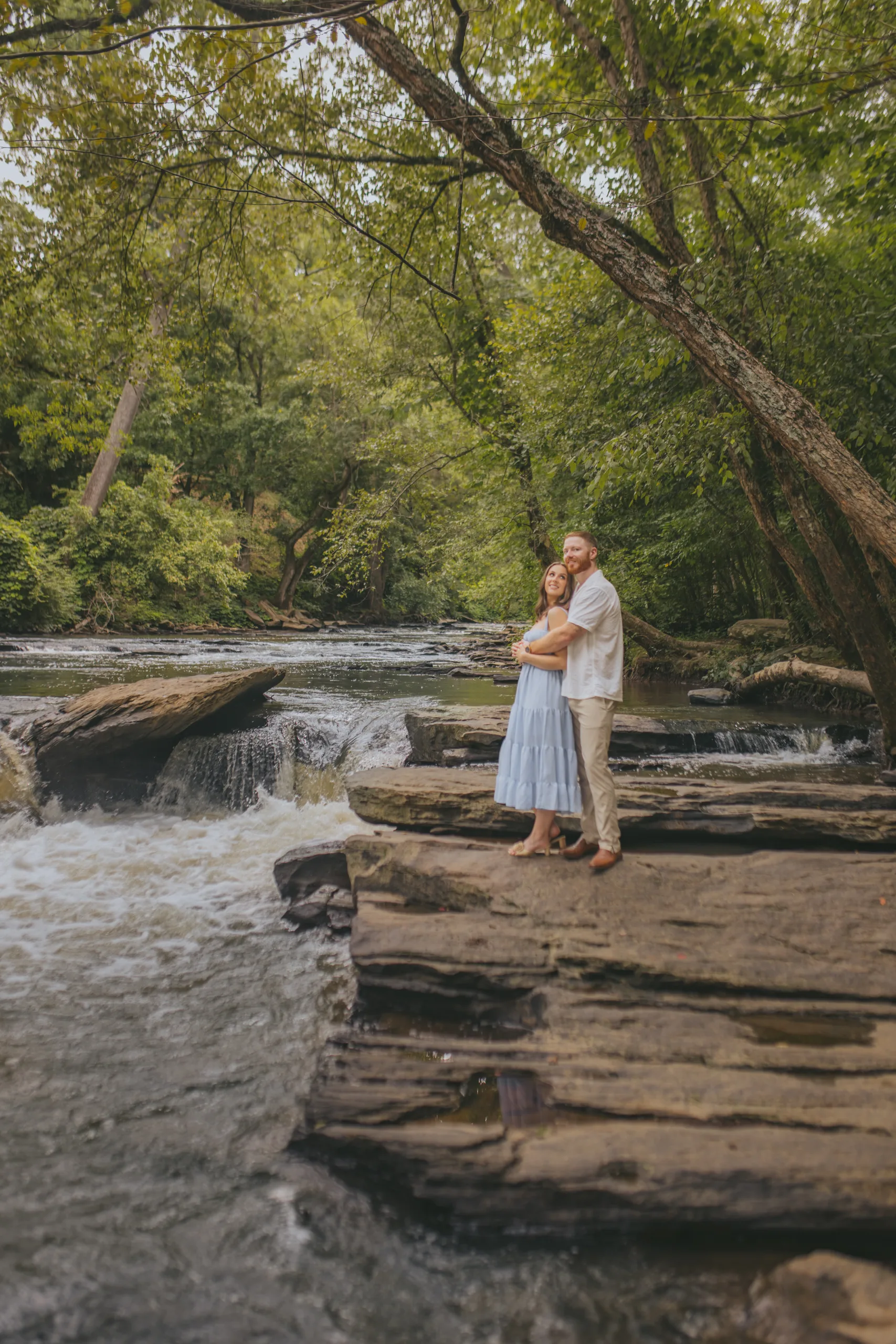 Engagement: on the rocks under the trees along Vickery Creek, at their engagement session at Roswell Mill in Roswell, GA