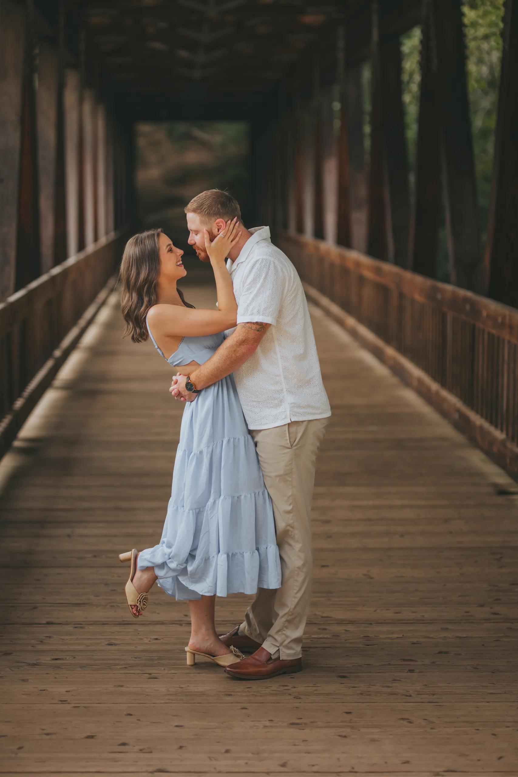 Engagement: her hand on his face on the covered bridge, at their engagement session at Roswell Mill in Roswell, GA