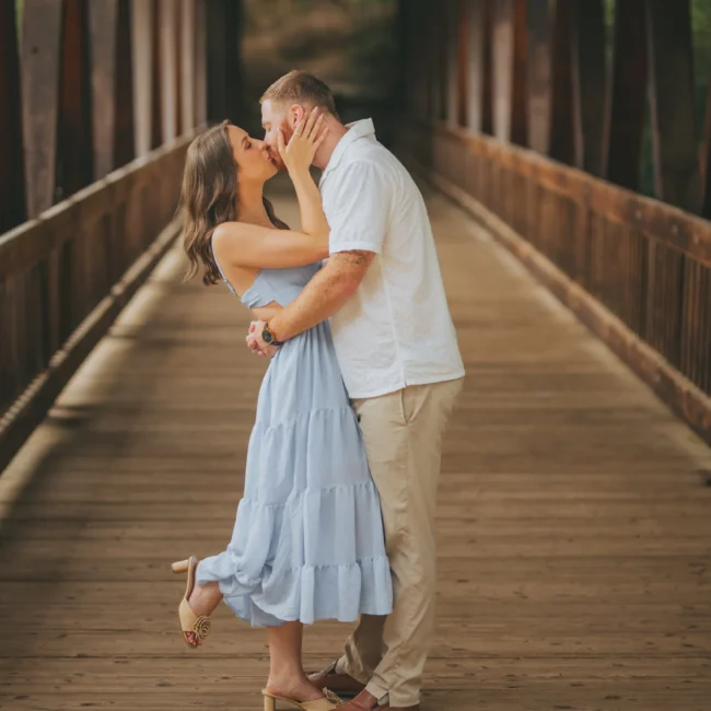 Engagement: a kiss on the covered bridge, at their engagement session at Roswell Mill in Roswell, GA