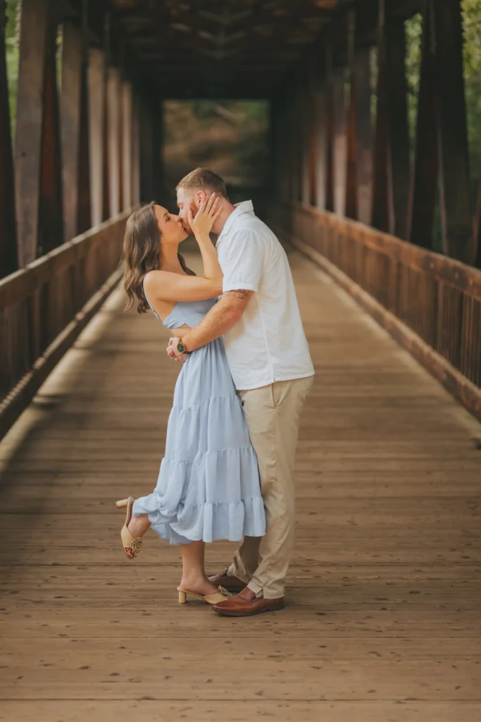 Engagement: a kiss on the covered bridge, at their engagement session at Roswell Mill in Roswell, GA