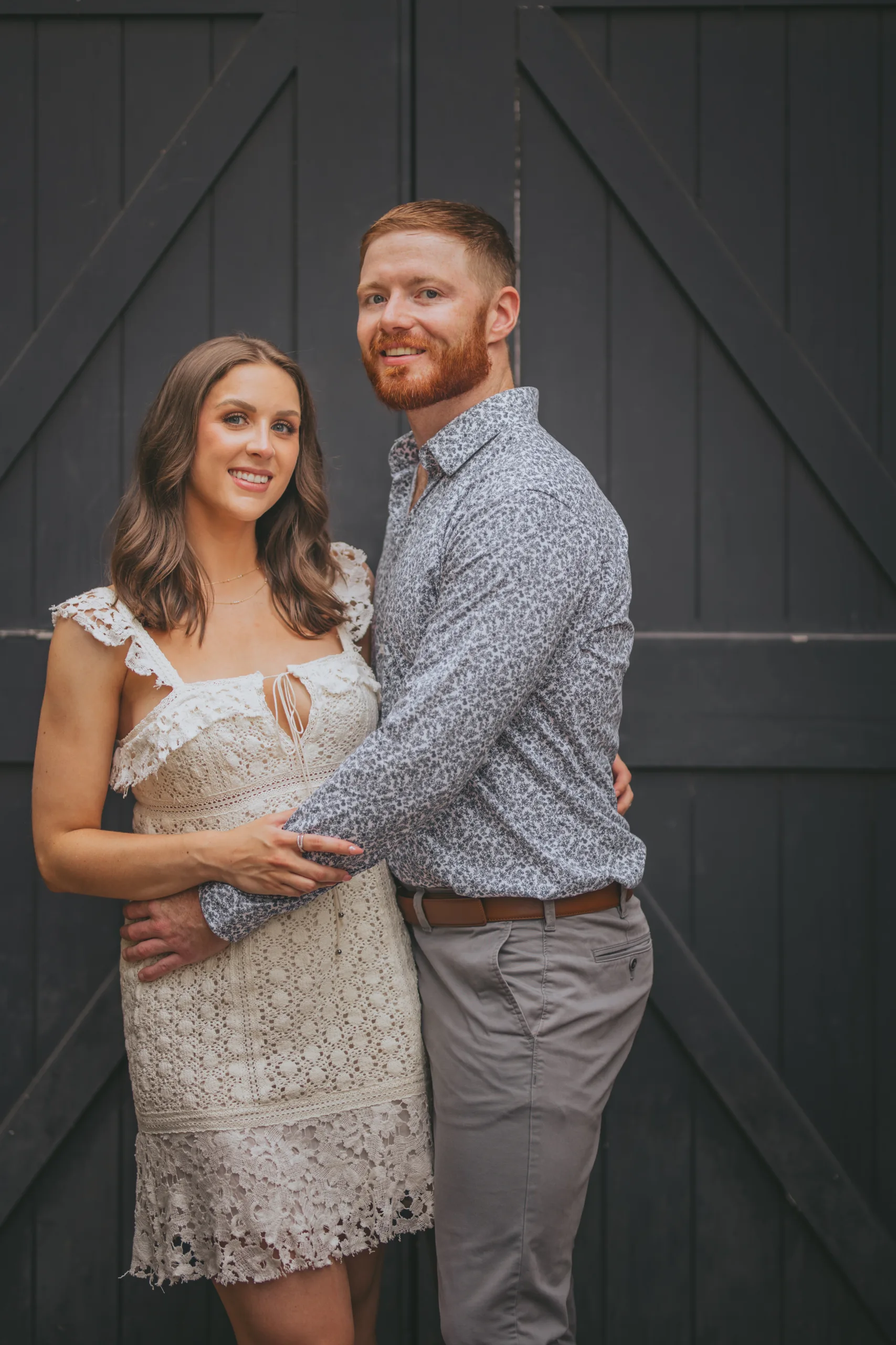 Engagement: smiling in front of the black barn doors, at their engagement session at Roswell Mill in Roswell, GA