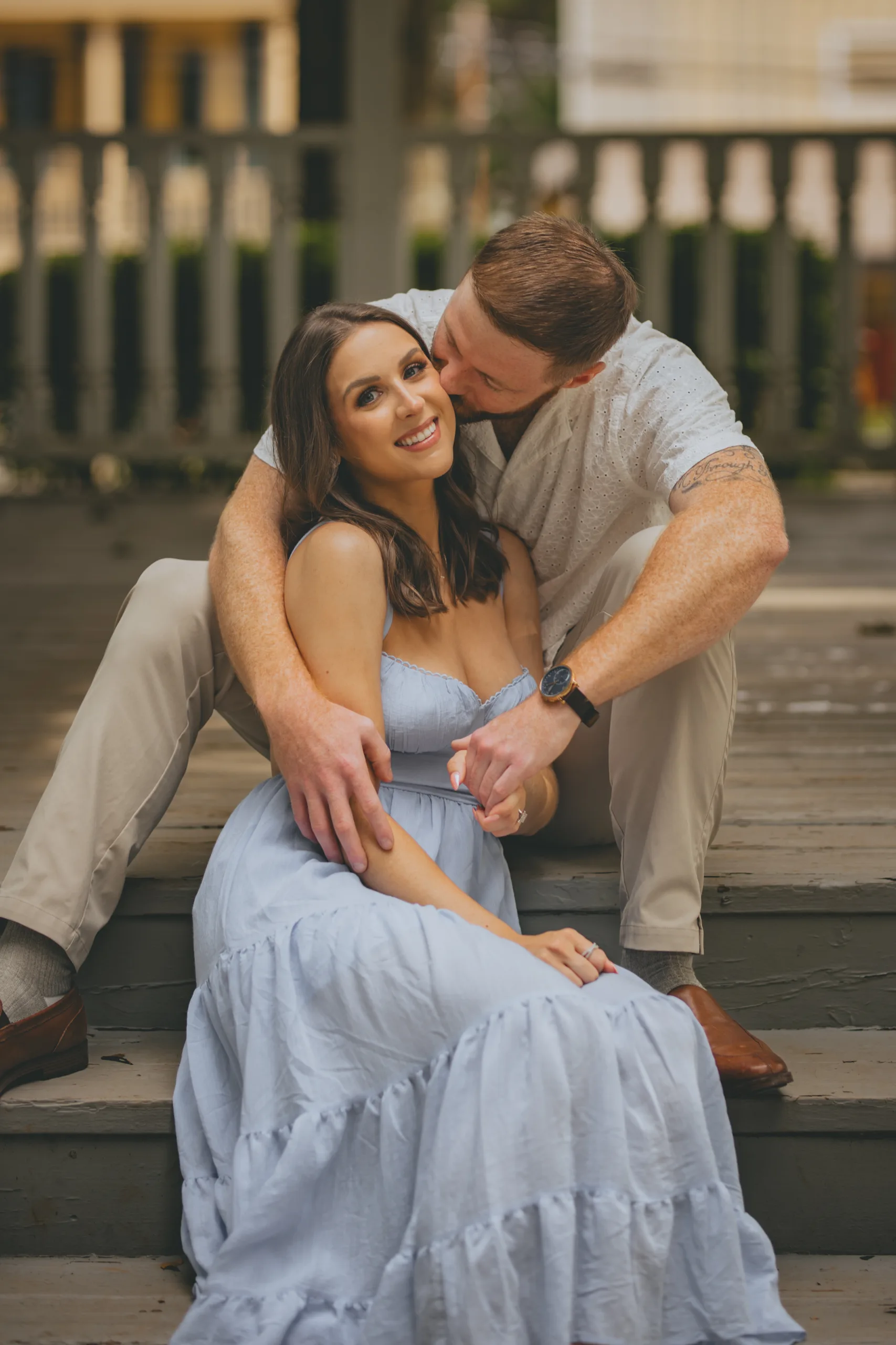 Engagement: a kiss on her head on the steps, at their engagement session on Roswell Square in Roswell, GA