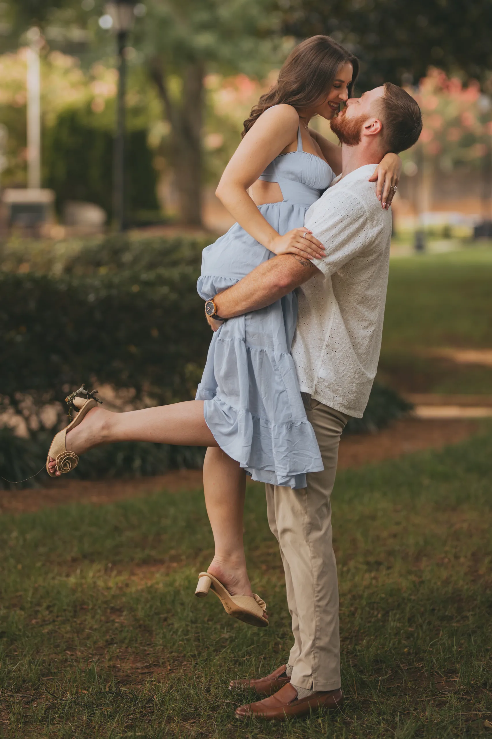 Engagement: him lifting her on the lawn, her heel kicked up, at their engagement session on Roswell Square in Roswell, GA