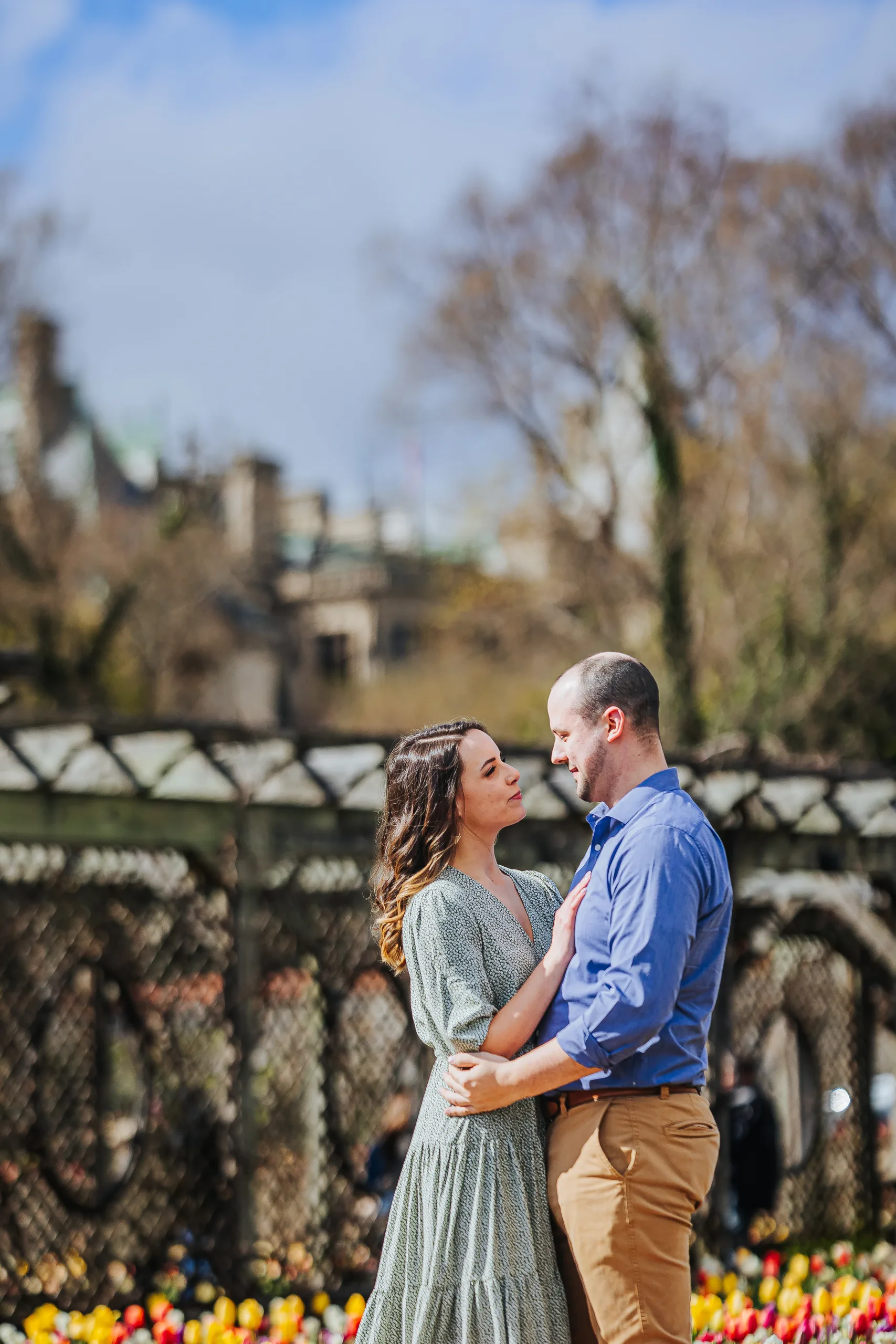 Walled Garden: holding each other by the tulip beds, the house rooftops behind them, at their engagement session at Biltmore Estate in Asheville, NC