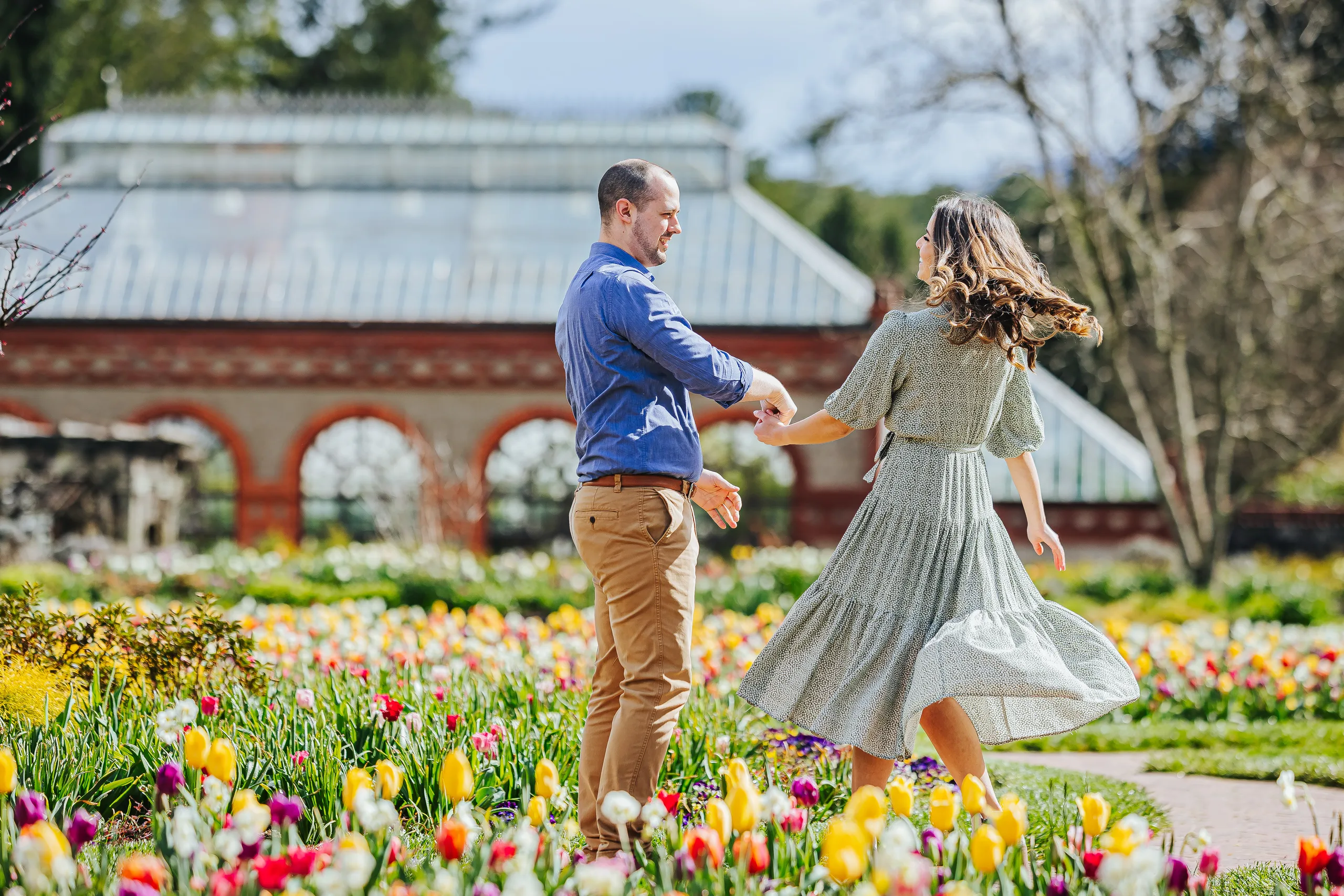 Walled Garden: him twirling her through the tulips, the Conservatory behind them, at their engagement session at Biltmore Estate in Asheville, NC