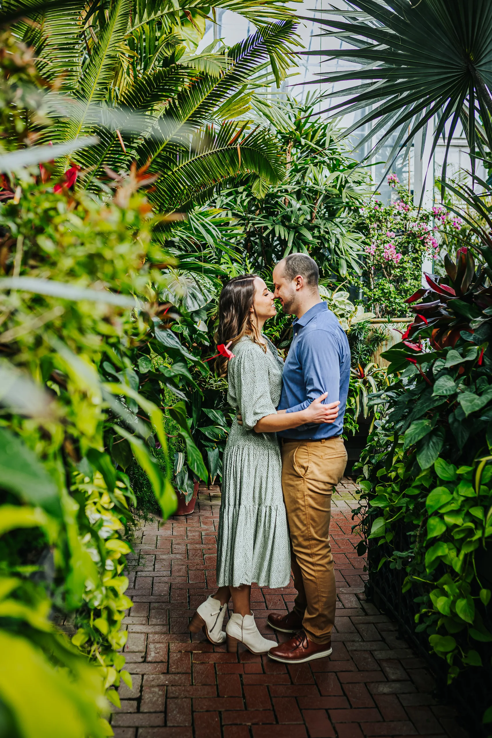 Conservatory: close together on the brick path between the palms, at their engagement session at Biltmore Estate in Asheville, NC