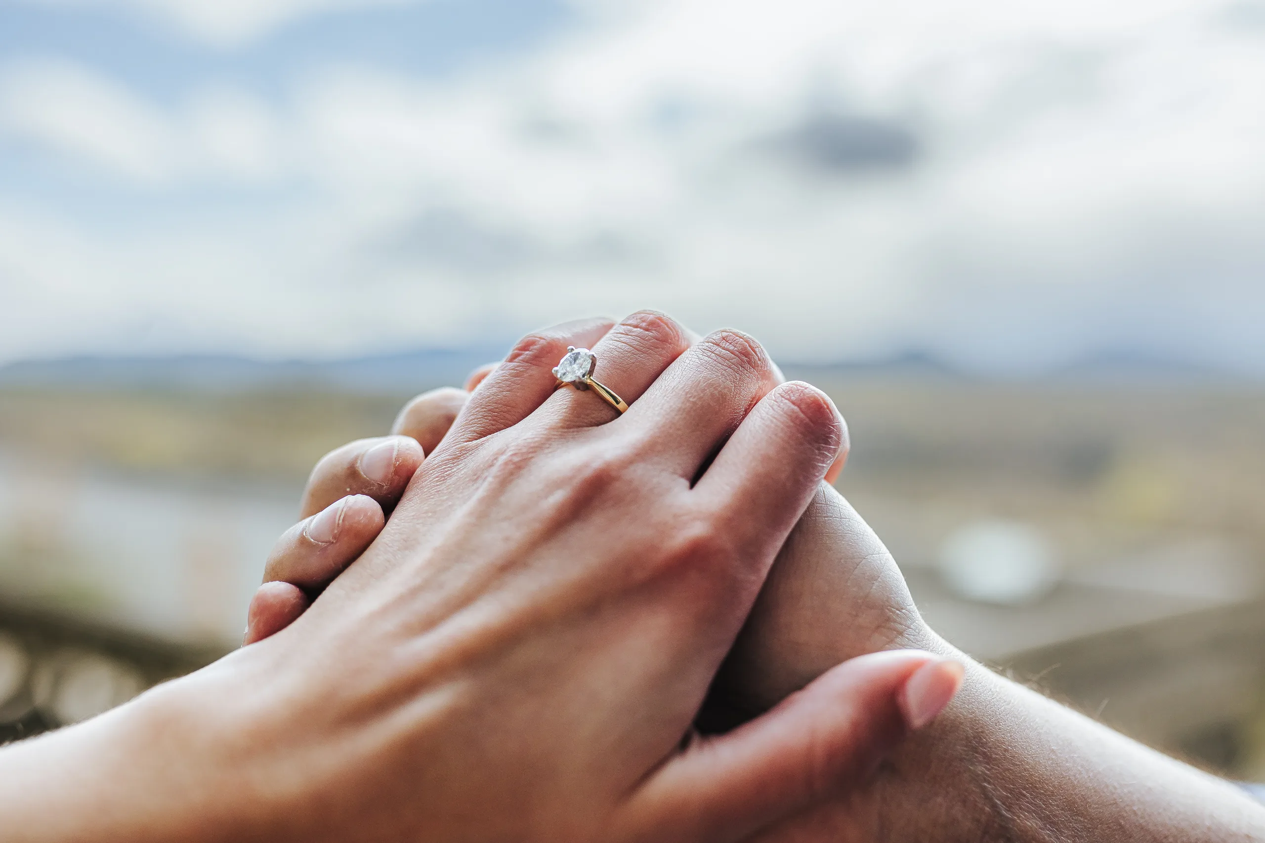 Engagement Ring: her hand and ring over his, the mountains blurred behind, at their engagement session at Biltmore Estate in Asheville, NC