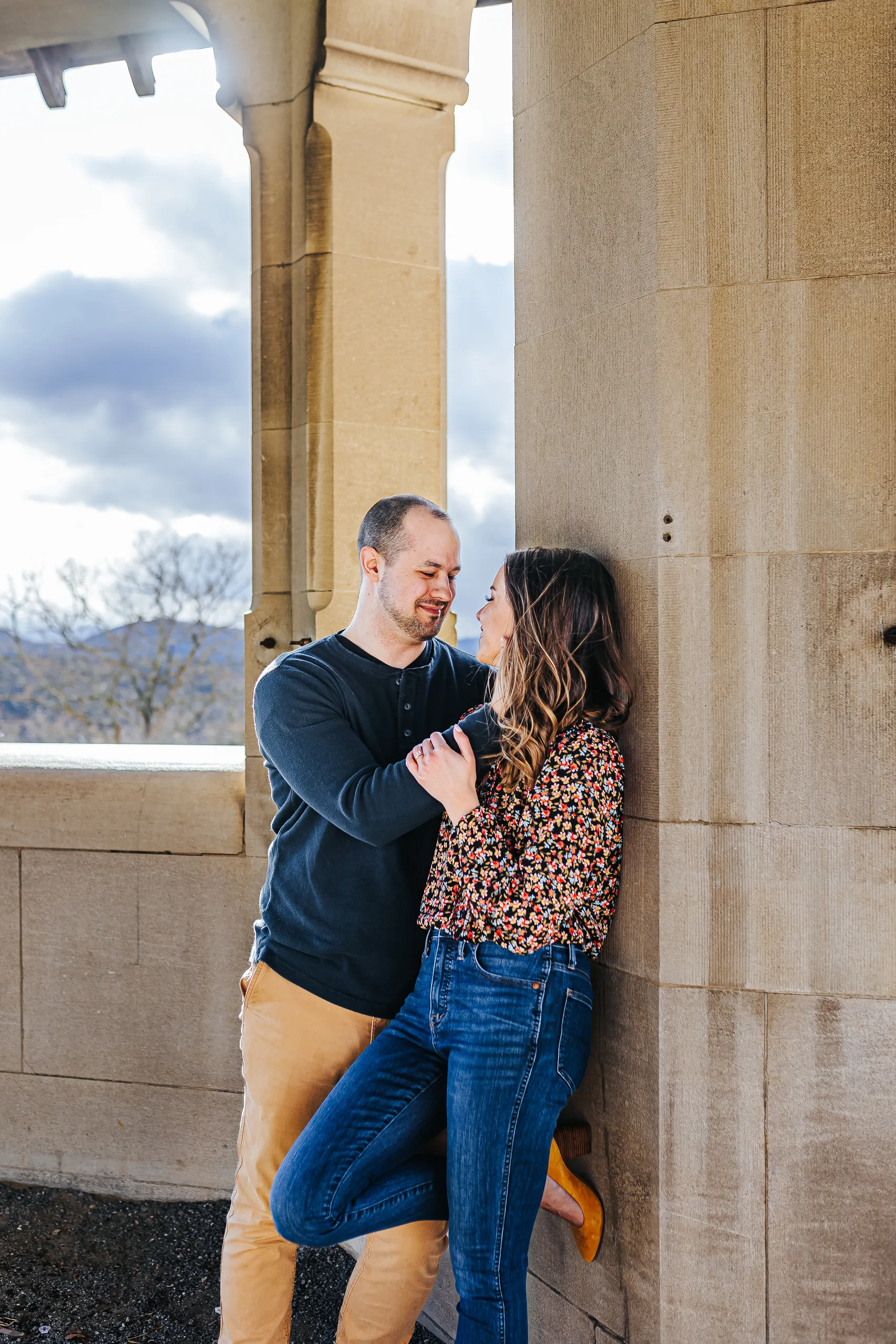 Terrace: leaning together against a stone column, the mountains beyond, at their engagement session at Biltmore Estate in Asheville, NC