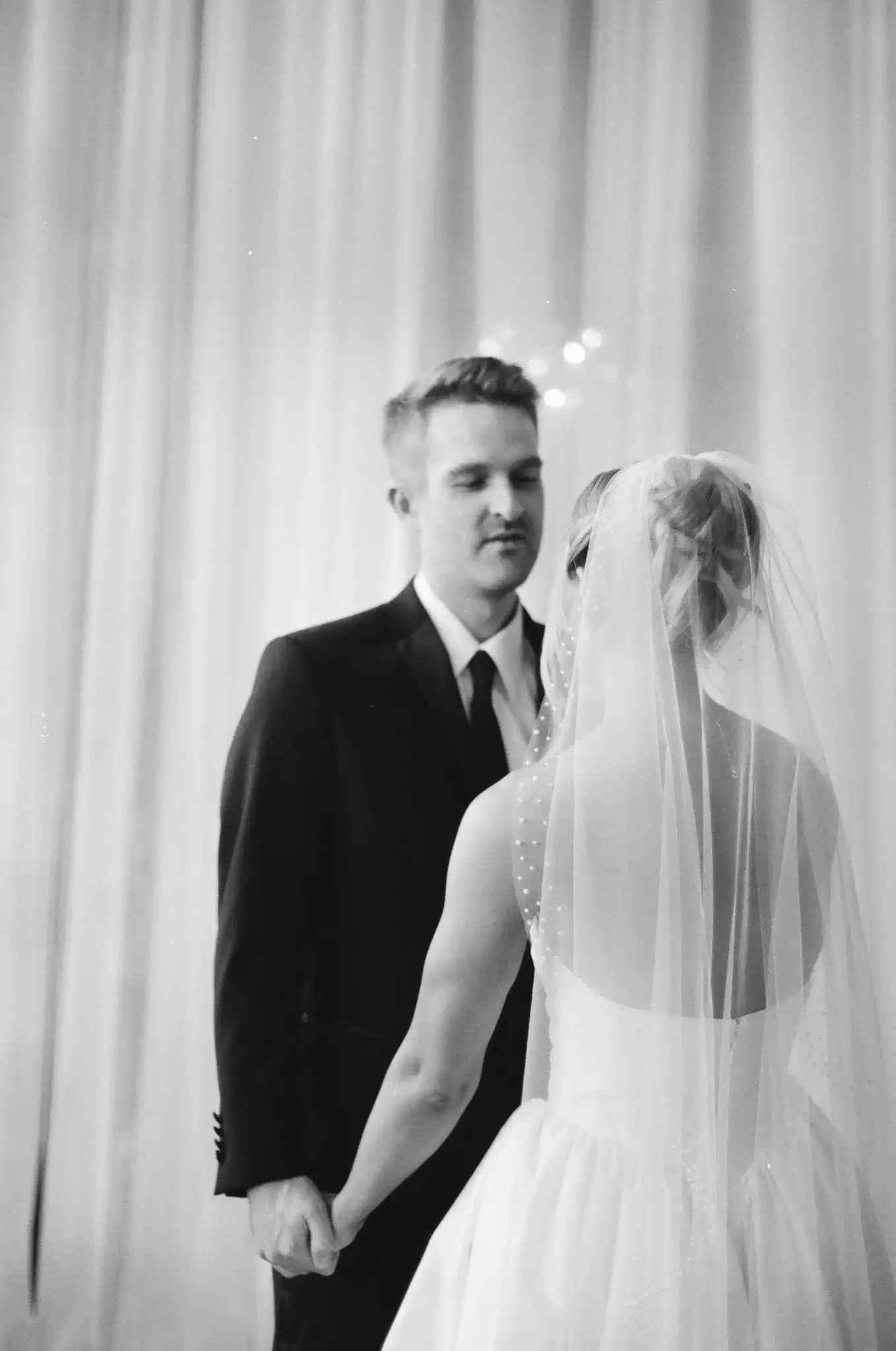 Bride and groom holding hands at their first look indoors, in black and white on 35mm film at The Venue at Sharp Mountain in Jasper, Georgia
