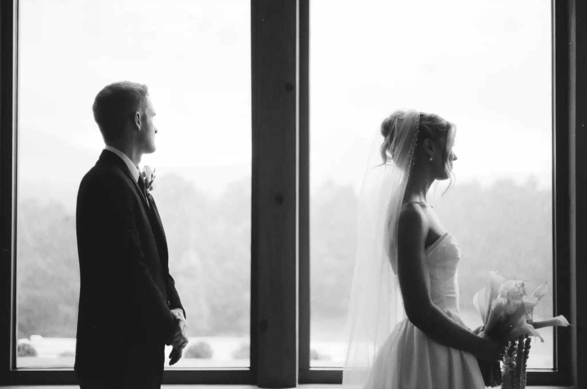 Bride and groom turned away from each other at the windows before their first look, in black and white on 35mm film at The Venue at Sharp Mountain in Jasper, Georgia