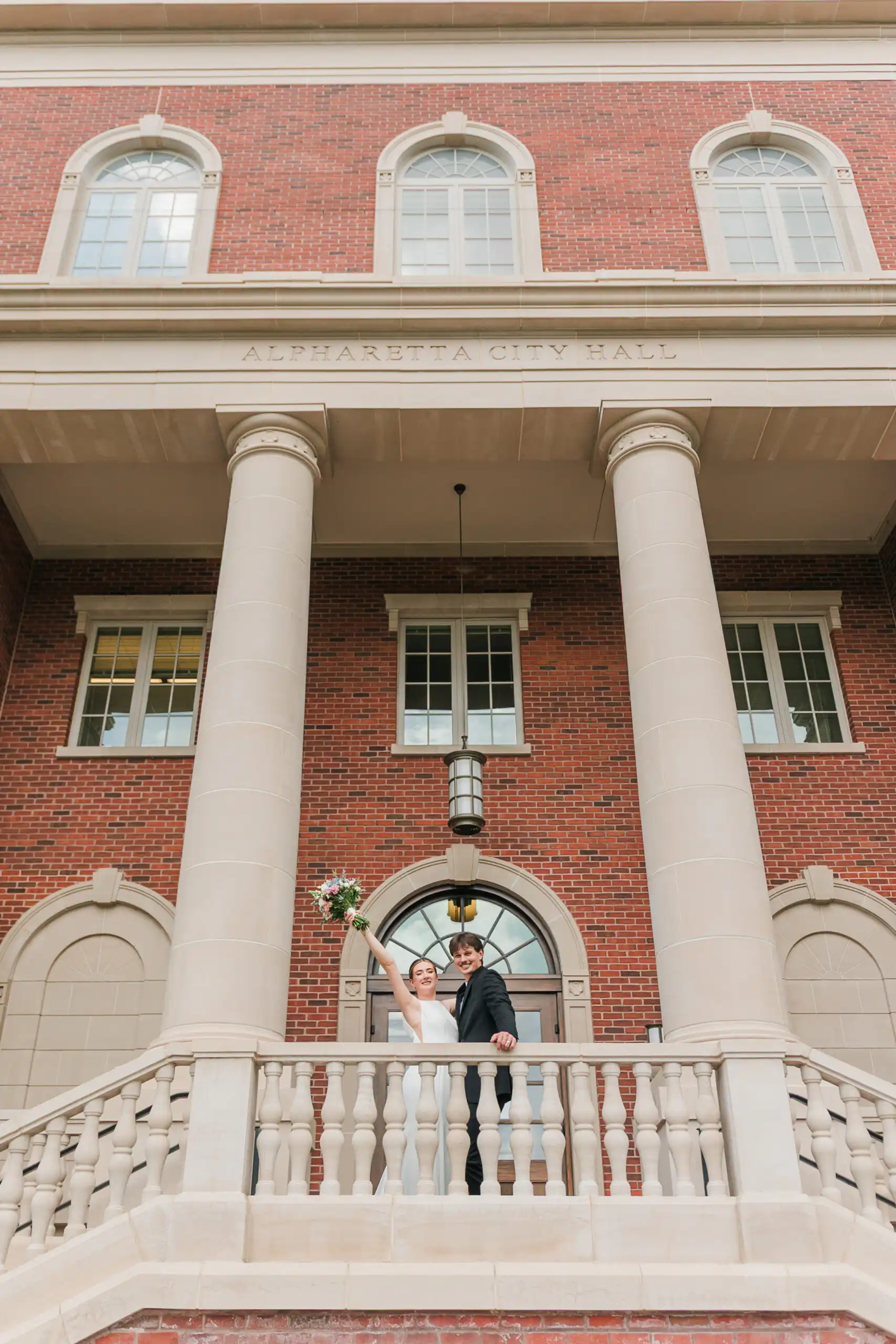 Wedding Formals: the two of them on the steps with her bouquet raised, at their elopement at Alpharetta City Hall in Alpharetta, GA
