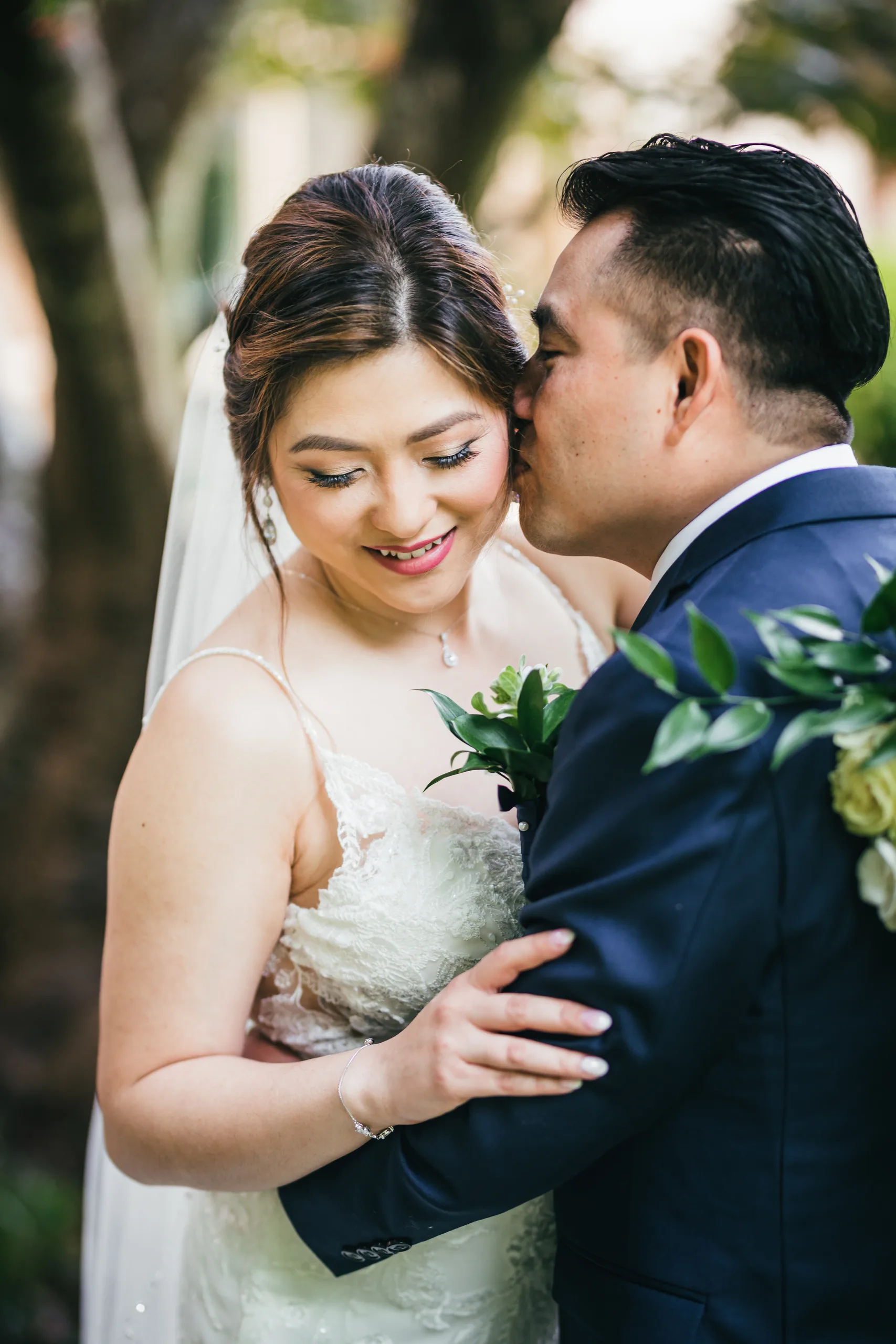 First Look: the groom kissing her cheek among the trees before their wedding at Holy Cross Catholic Church in Atlanta, GA