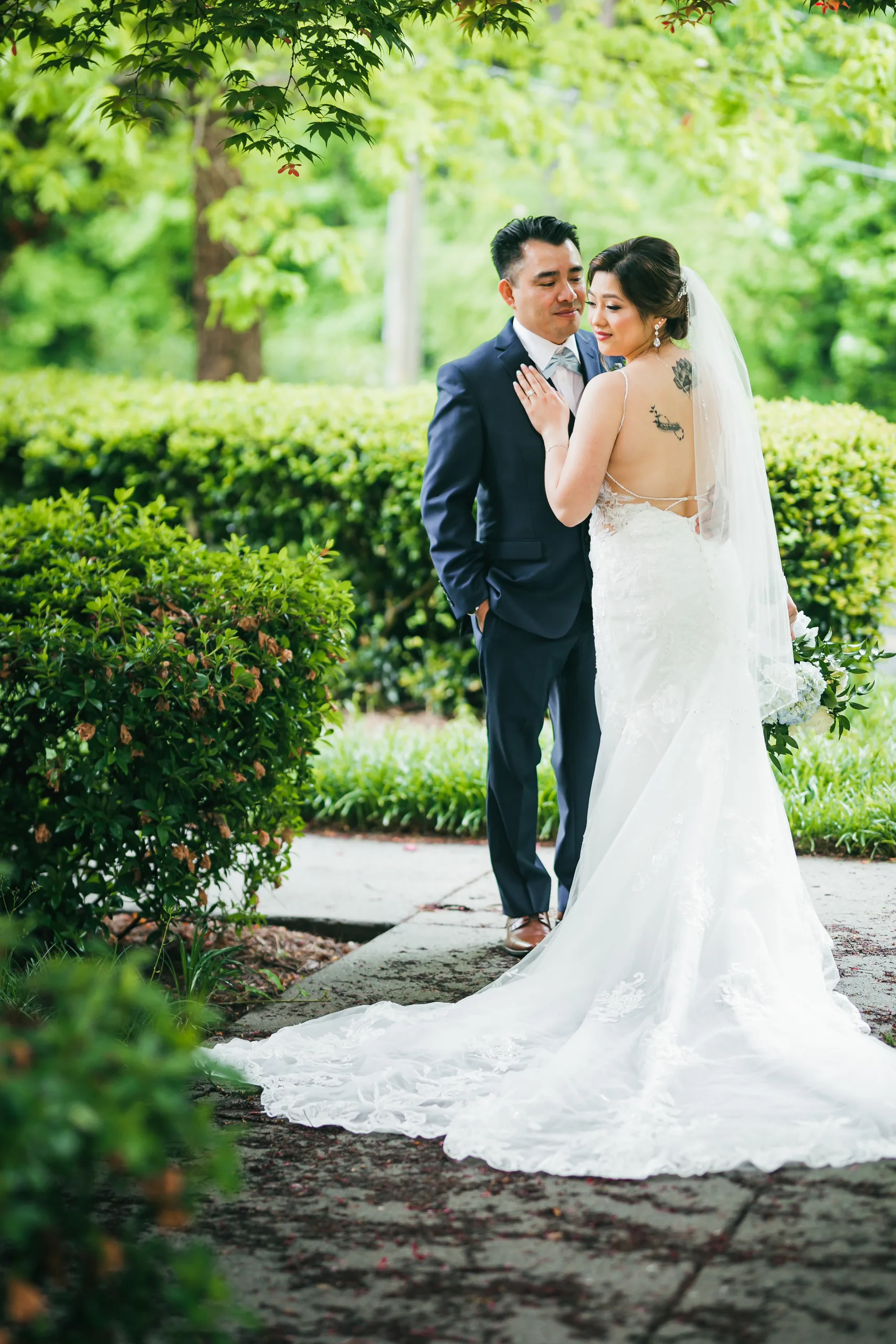 First Look: the couple on the garden path with her train behind her before their wedding at Holy Cross Catholic Church in Atlanta, GA