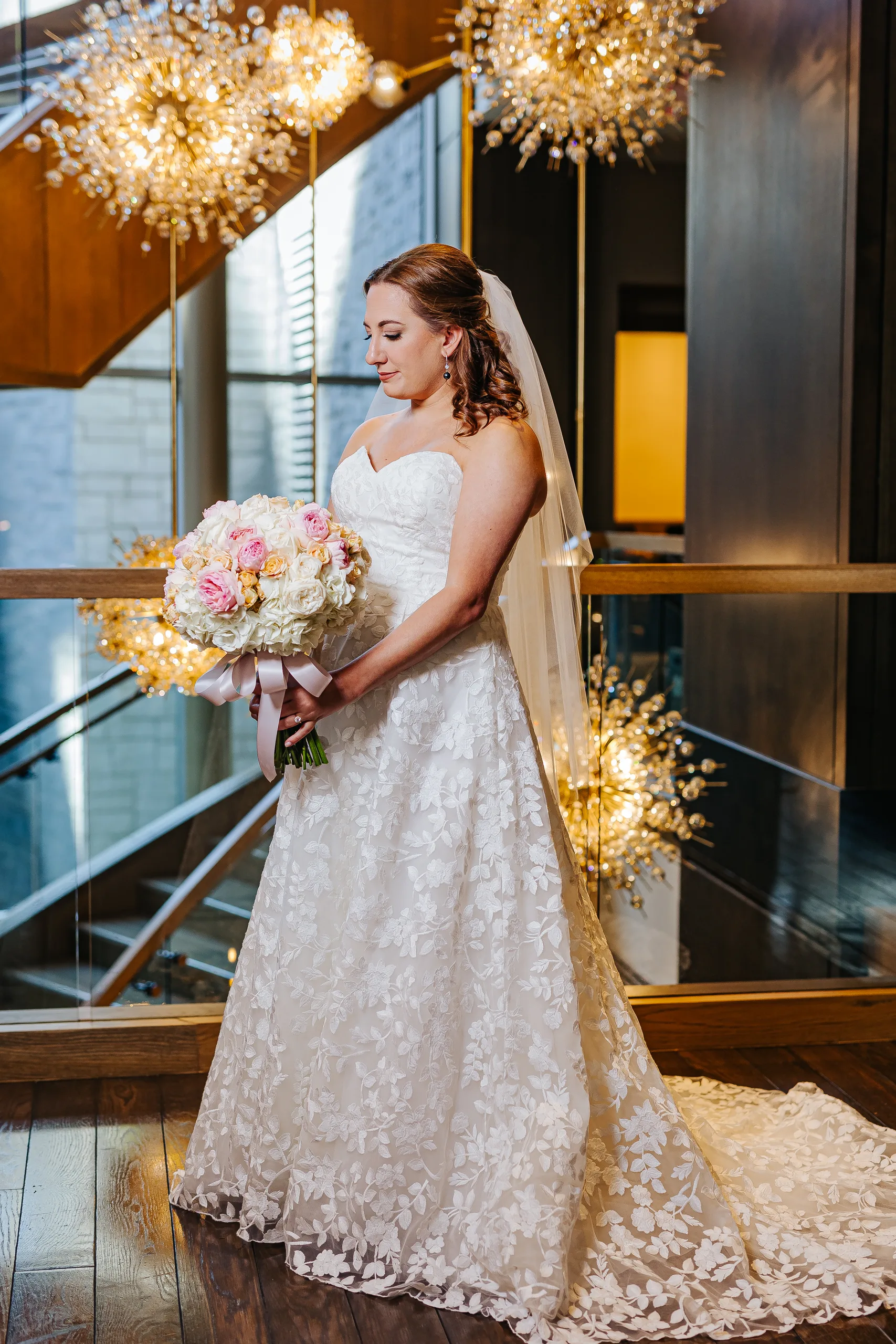 Bridal Portraits: the bride with her bouquet under the chandelier by the staircase at their wedding at the Omni Hotel at The Battery in Atlanta, GA