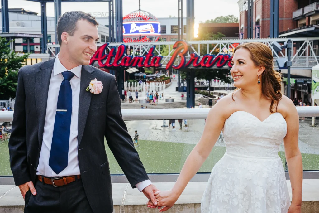 Wedding Formals: holding hands in front of the Atlanta Braves sign at their wedding at the Omni Hotel at The Battery in Atlanta, GA