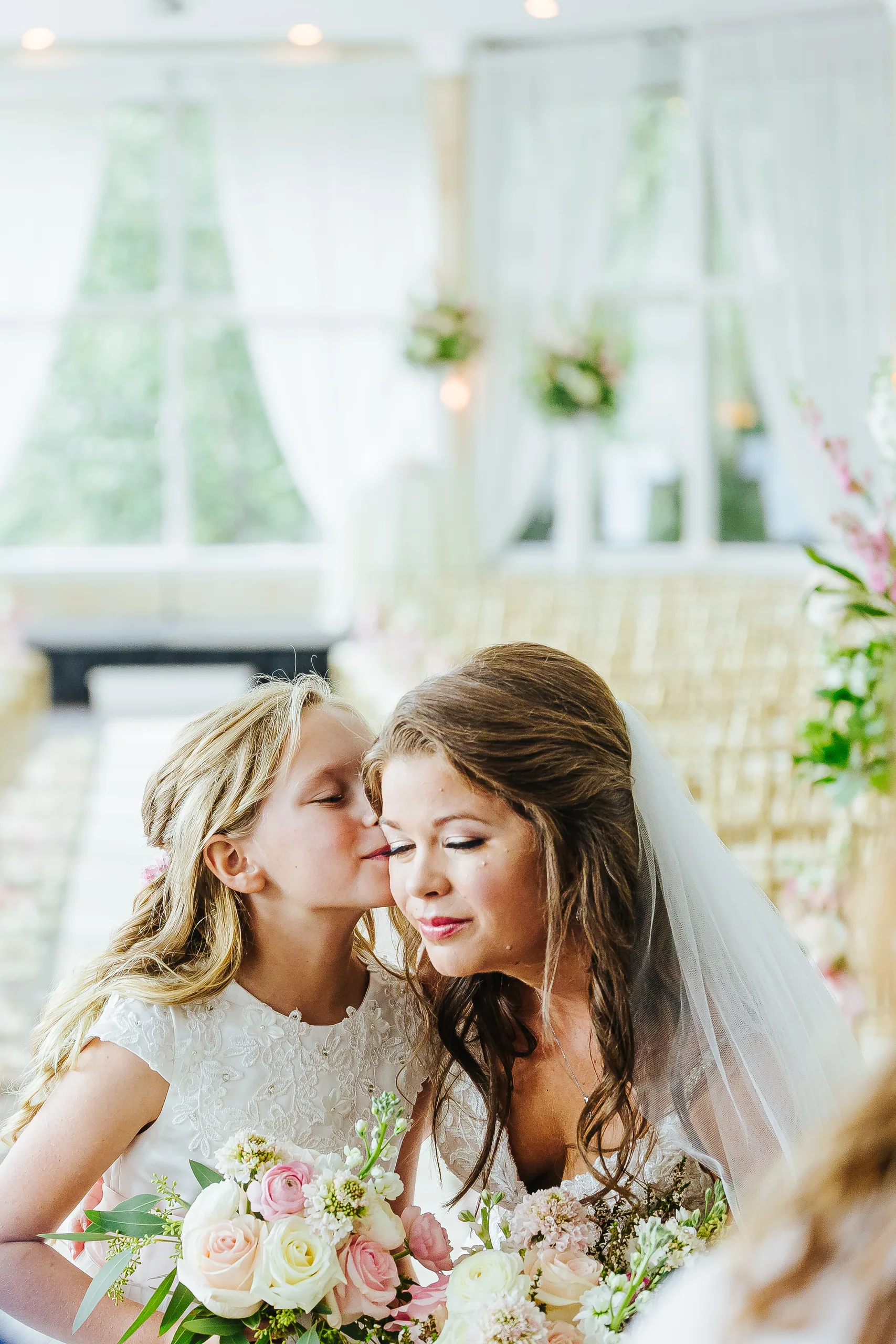 Bridal Portraits: a flower girl kissing the bride on the cheek, at their wedding at The Piedmont Room in Atlanta, GA