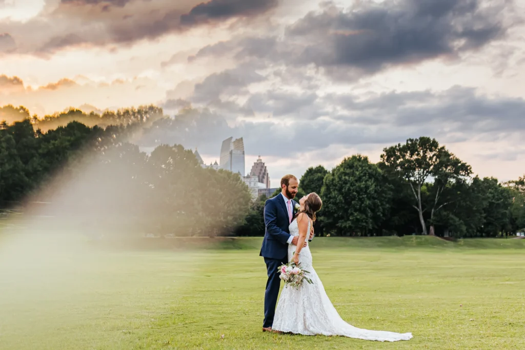 Wedding Formals: a kiss at sunset with the Midtown skyline on the meadow in Piedmont Park, at their wedding at The Piedmont Room in Atlanta, GA