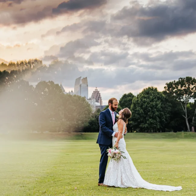 Wedding Formals: a kiss at sunset with the Midtown skyline on the meadow in Piedmont Park, at their wedding at The Piedmont Room in Atlanta, GA