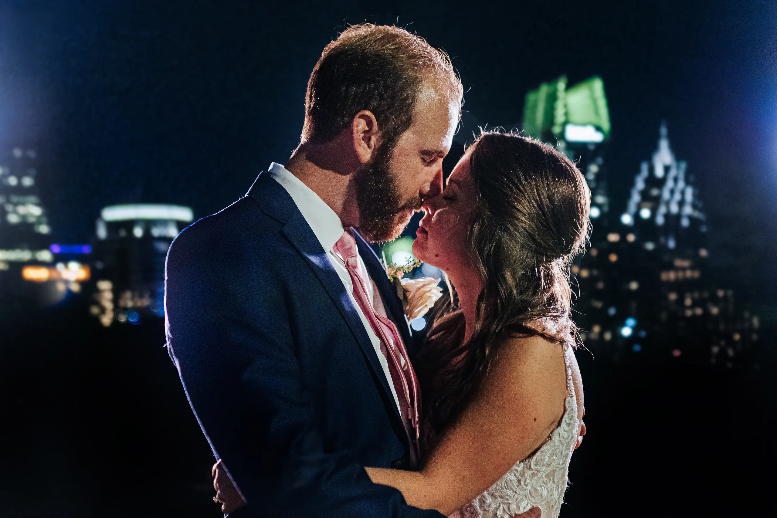 Wedding Formals: a kiss at night with the Midtown skyline lit up behind them, at their wedding at The Piedmont Room in Atlanta, GA