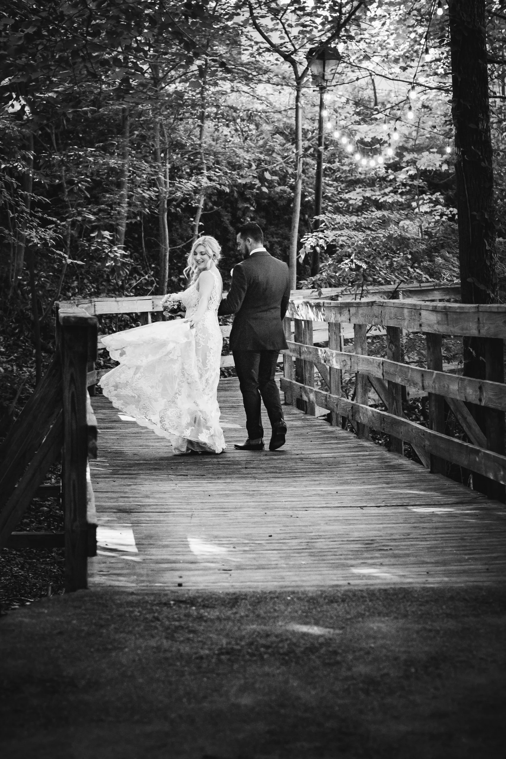 Wedding Formals: twirling her gown on a wooden footbridge, in black and white, at their wedding at Atlanta Evergreen Lakeside Resort in Stone Mountain, GA
