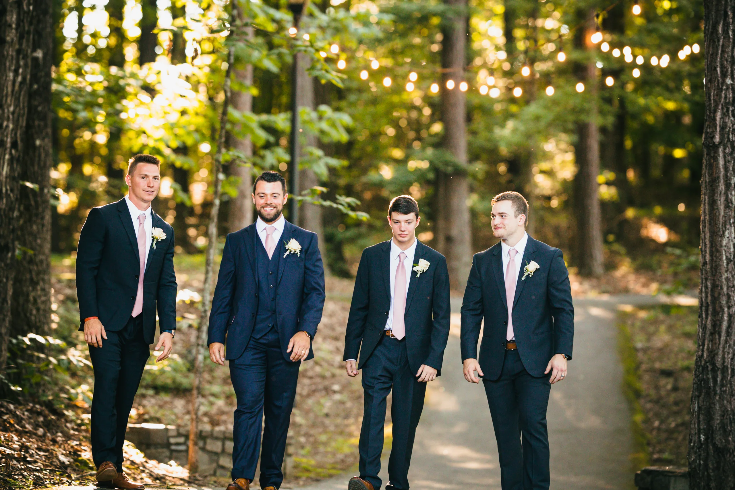 Wedding Party: the groom and his groomsmen walking under the string lights, at their wedding at Atlanta Evergreen Lakeside Resort in Stone Mountain, GA