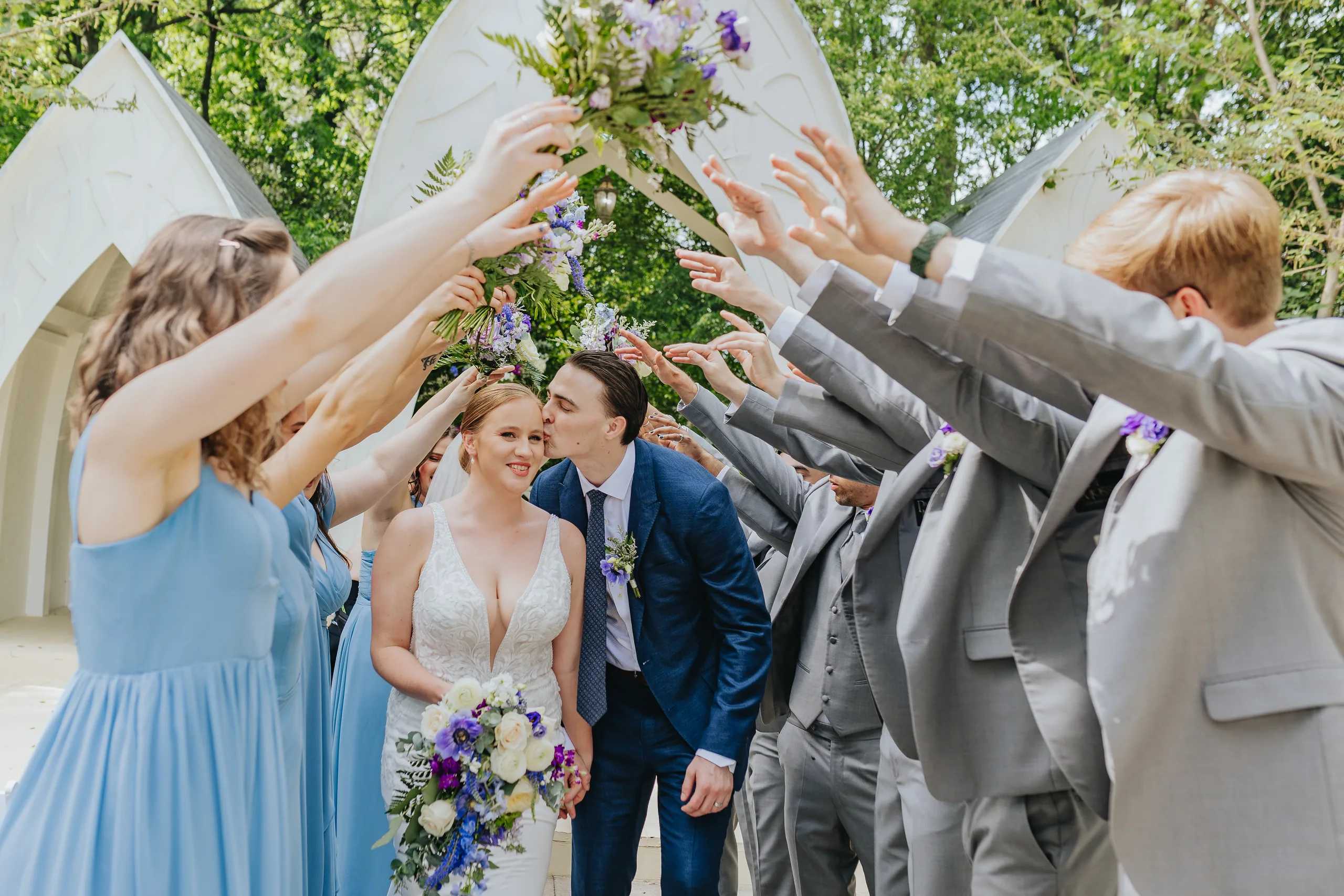 Wedding Party: a kiss under an arch of bouquets, at their wedding at The Wildflower 301 in Greensboro, GA