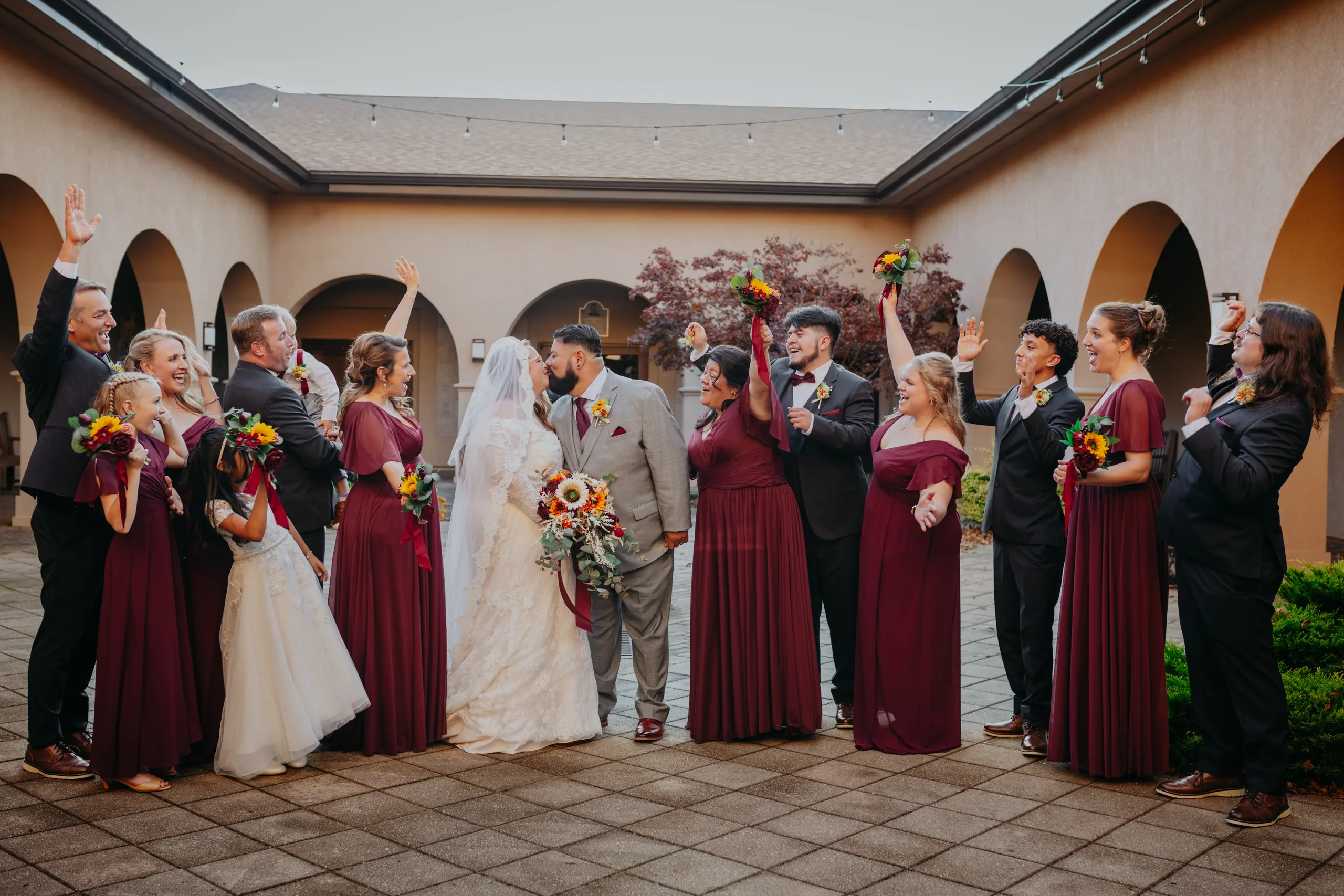 Wedding Party: a kiss as the wedding party cheers in the courtyard, at their wedding at St. Lawrence Catholic Church in Lawrenceville, GA