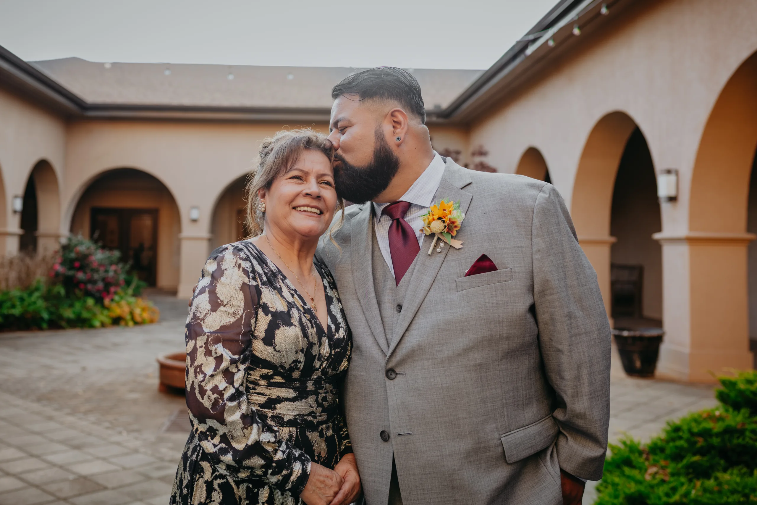 Family Formals: the groom kissing his mom on the head in the courtyard, at their wedding at St. Lawrence Catholic Church in Lawrenceville, GA