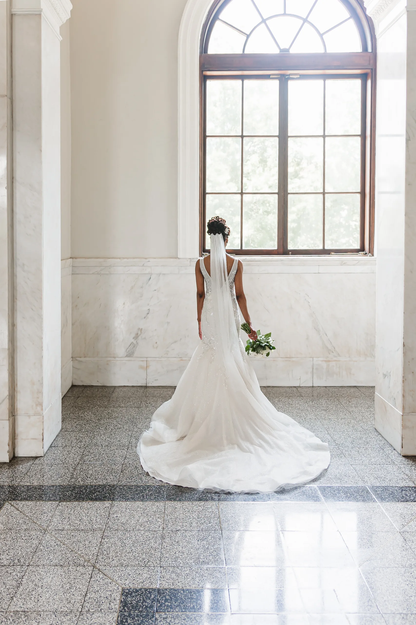 Bridal Portraits: the bride from behind under the arched window, her train spread out, at their wedding at the Historic DeKalb Courthouse in Decatur, GA