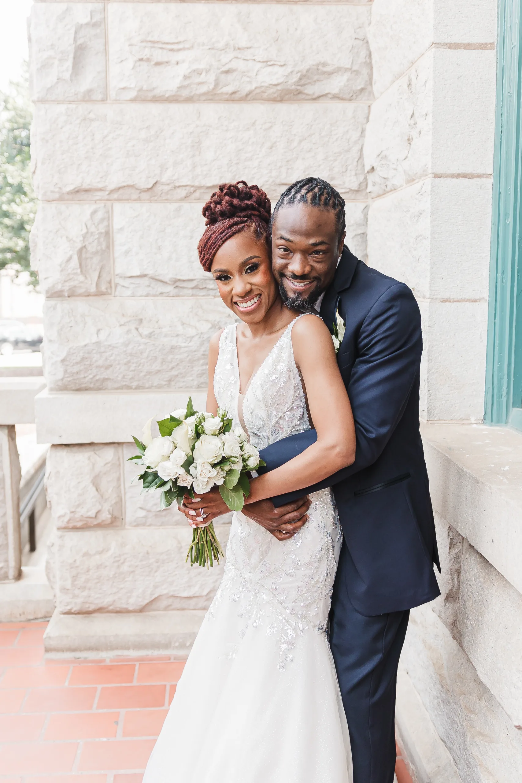 Wedding Formals: the groom hugging her from behind against the stone wall outside, at their wedding at the Historic DeKalb Courthouse in Decatur, GA