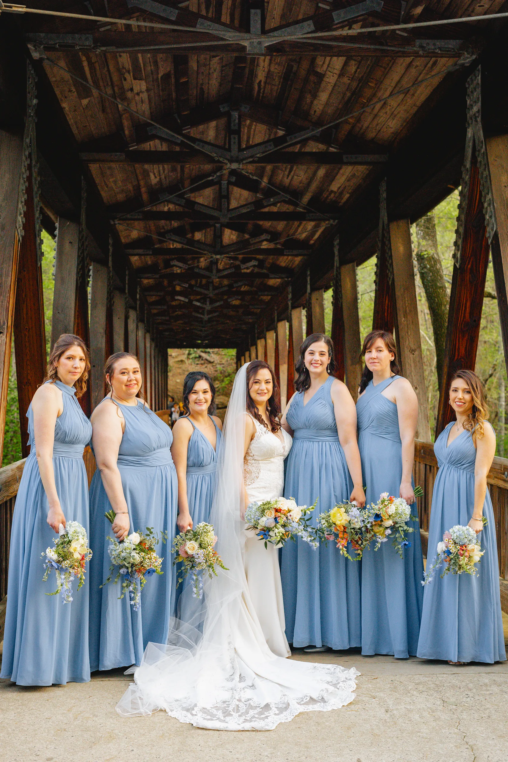 Wedding Party: the bride and her bridesmaids on the covered bridge at their wedding at Ivy Hall at Roswell Mill in Roswell, GA