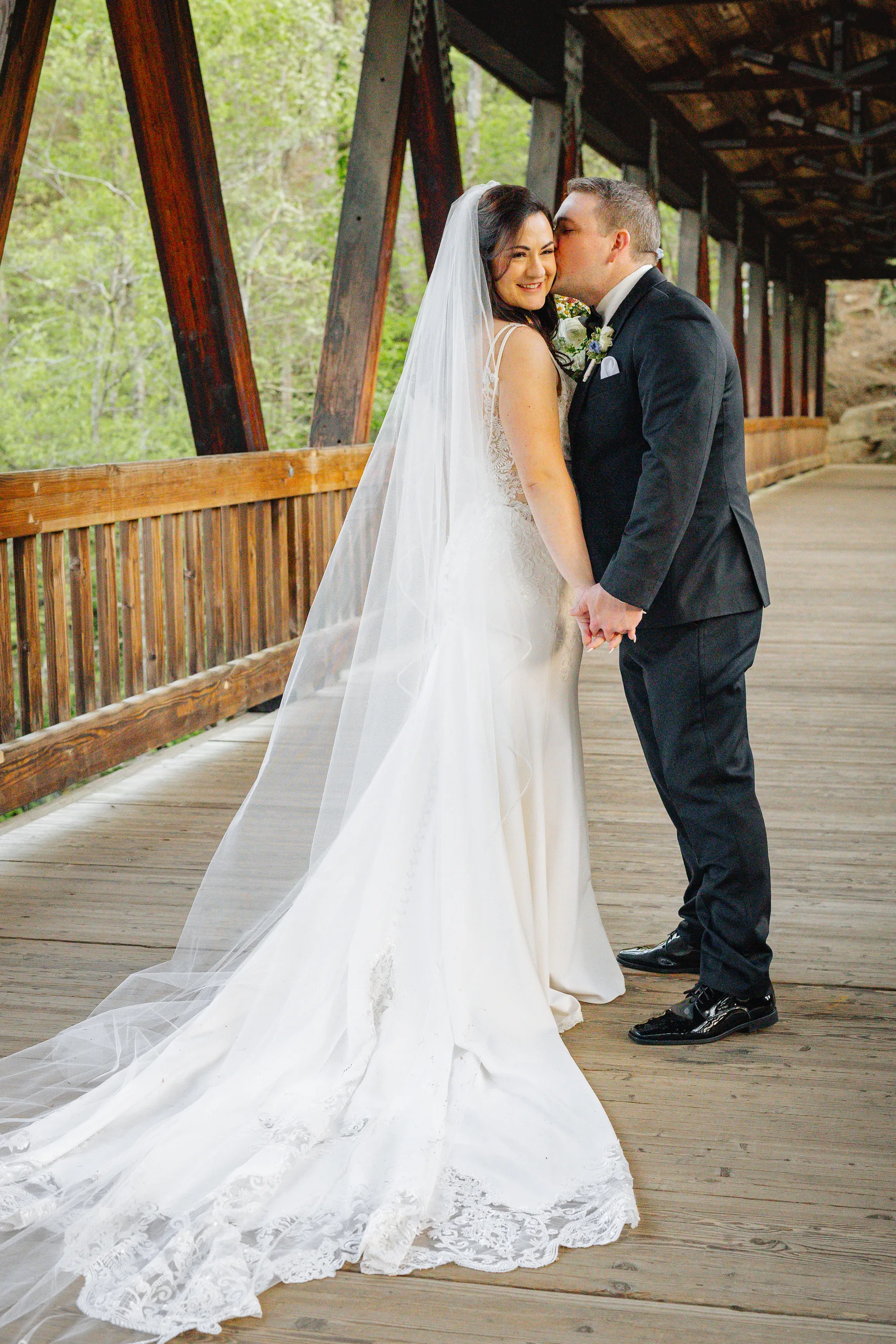 Wedding Formals: a kiss on the cheek on the covered bridge at their wedding at Ivy Hall at Roswell Mill in Roswell, GA