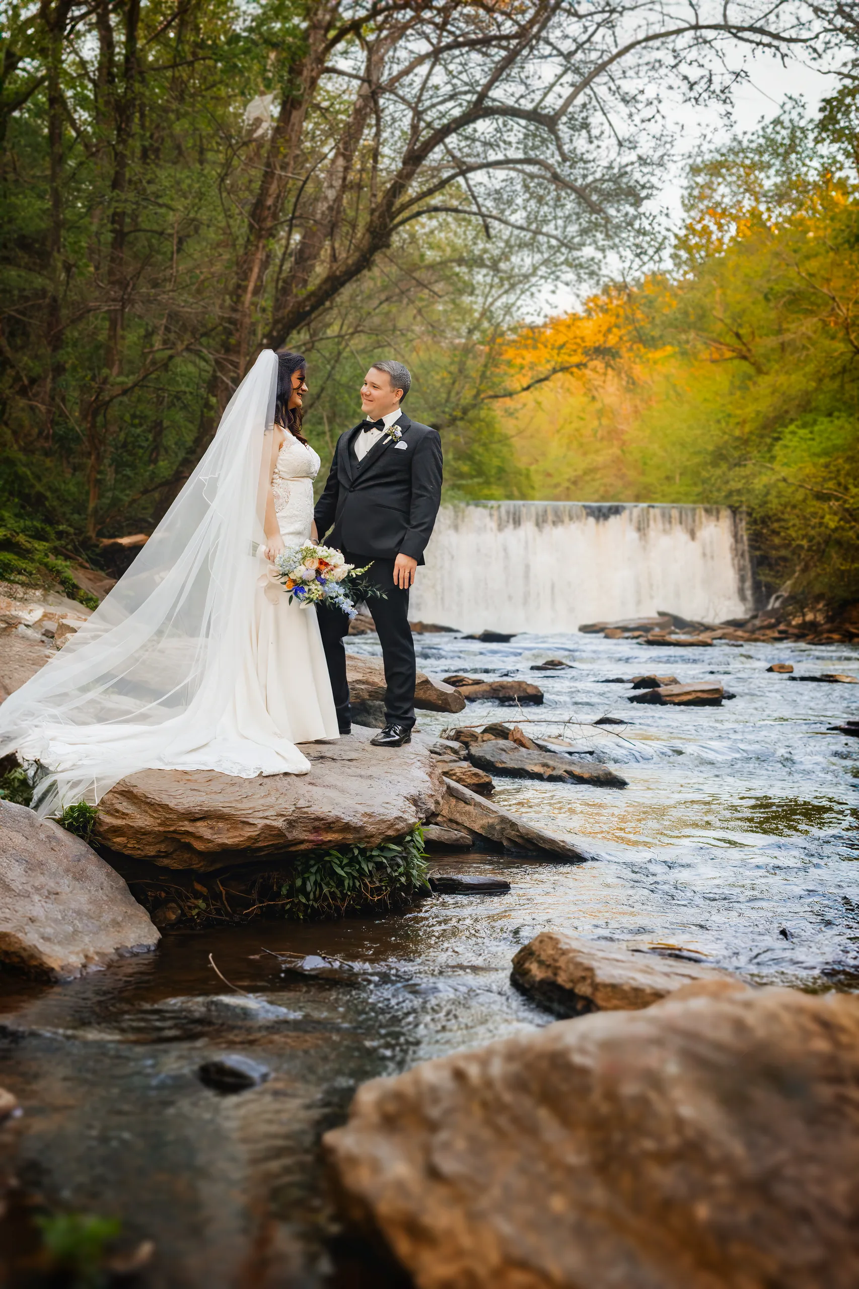 Wedding Formals: standing on the rocks with the falls behind them at their wedding at Ivy Hall at Roswell Mill in Roswell, GA