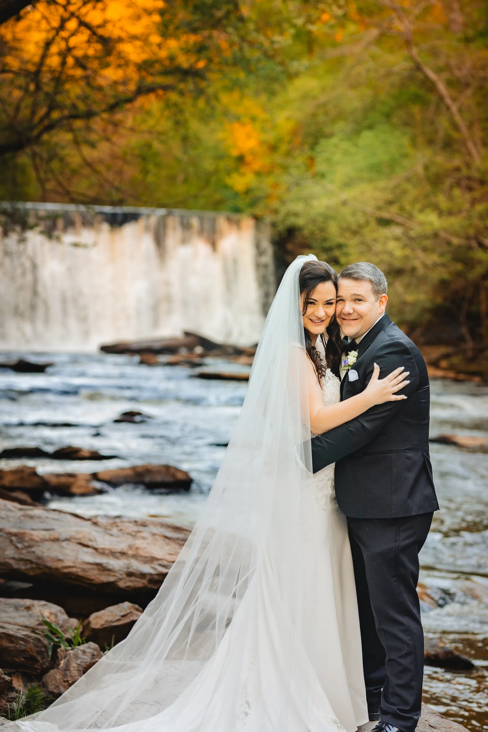 Wedding Formals: an embrace in front of Vickery Creek falls at their wedding at Ivy Hall at Roswell Mill in Roswell, GA