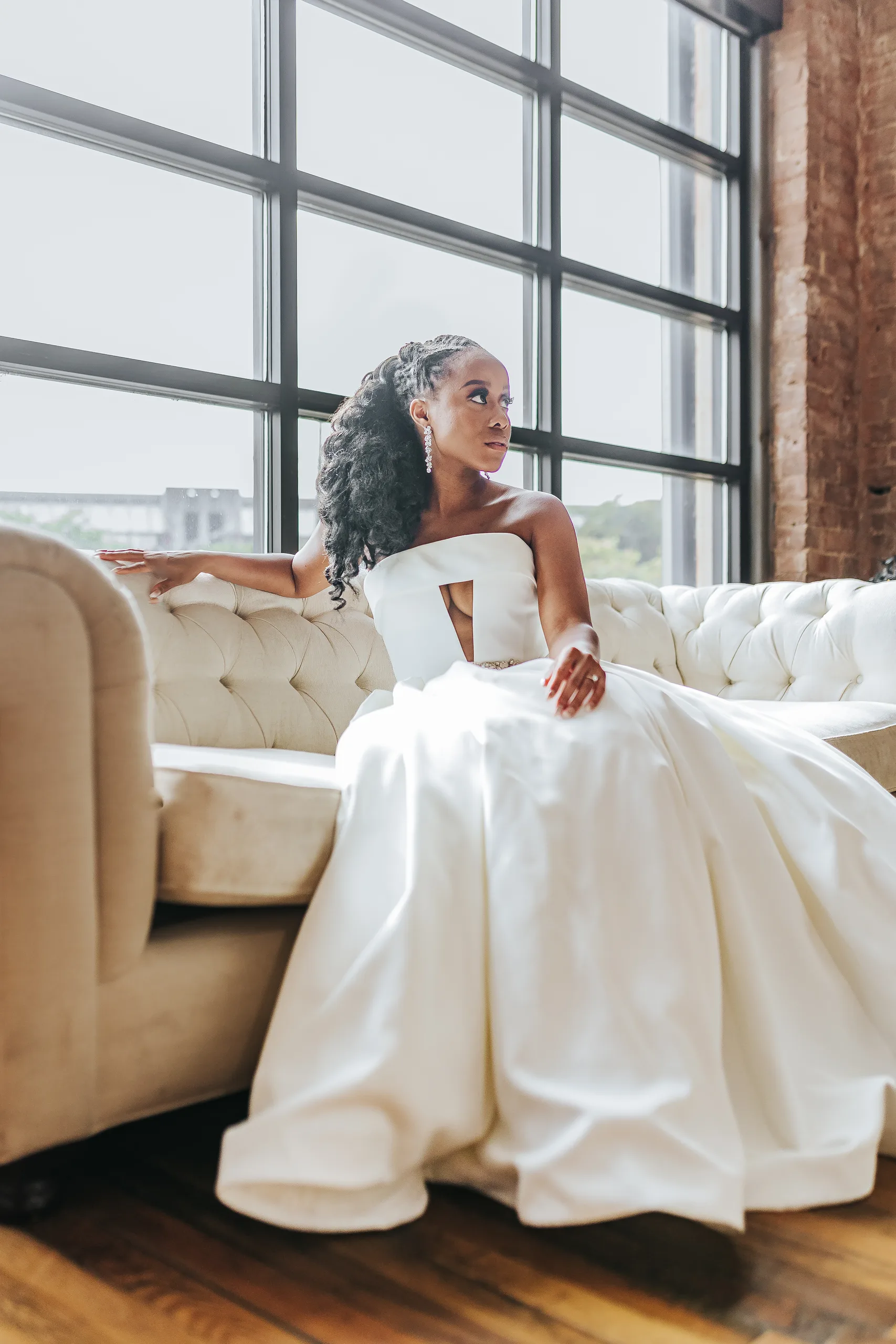 Bridal Portraits: the bride on the sofa with her gown spread out by the windows, at their wedding at Terminus 330 in Atlanta, GA