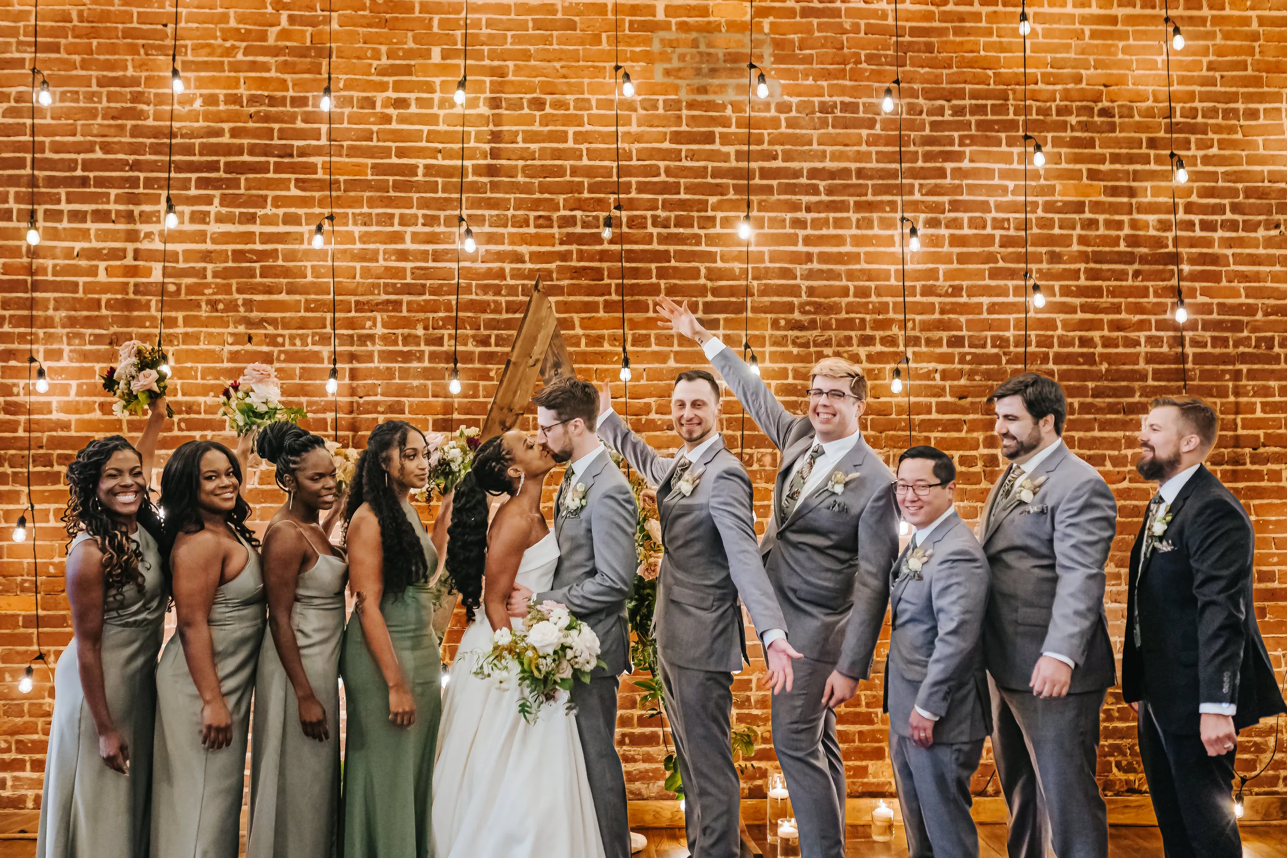 Wedding Party: everyone cheering in front of the brick wall, at their wedding at Terminus 330 in Atlanta, GA