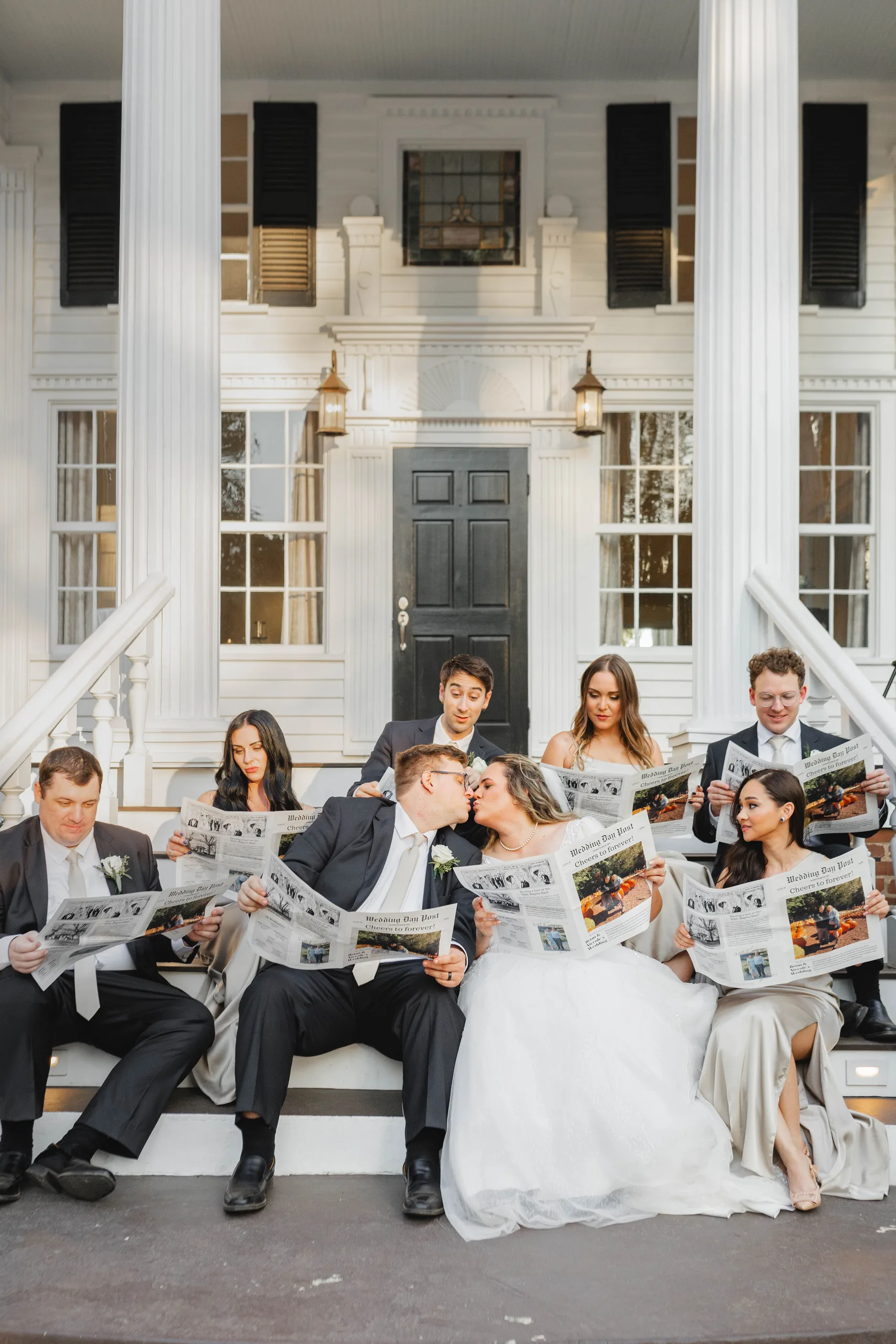 Wedding Party: everyone on the front steps reading the newspaper, the couple kissing behind theirs, at their wedding at Naylor Hall in Roswell, GA