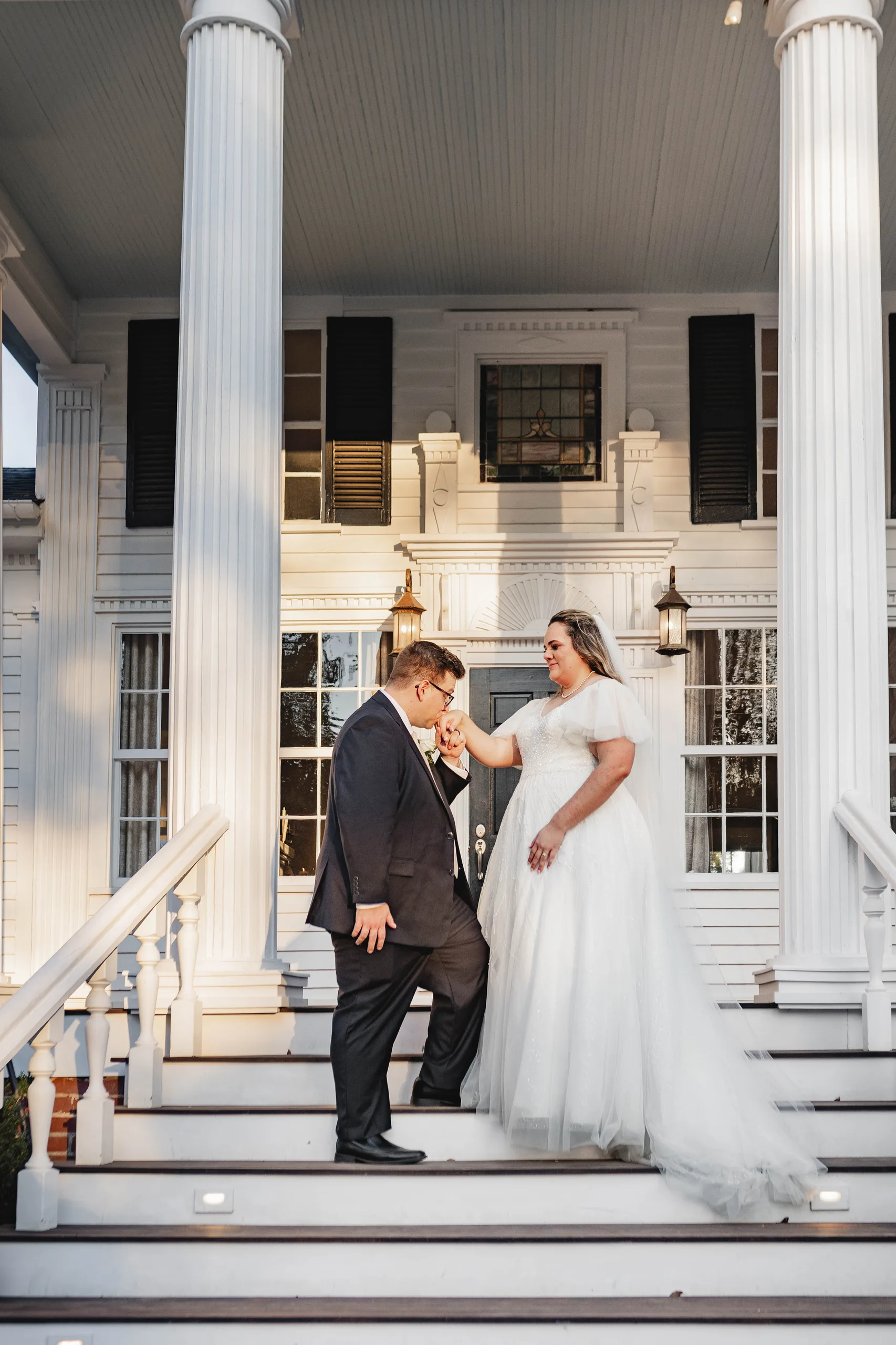 Wedding Formals: the groom kissing her hand on the front steps, at their wedding at Naylor Hall in Roswell, GA