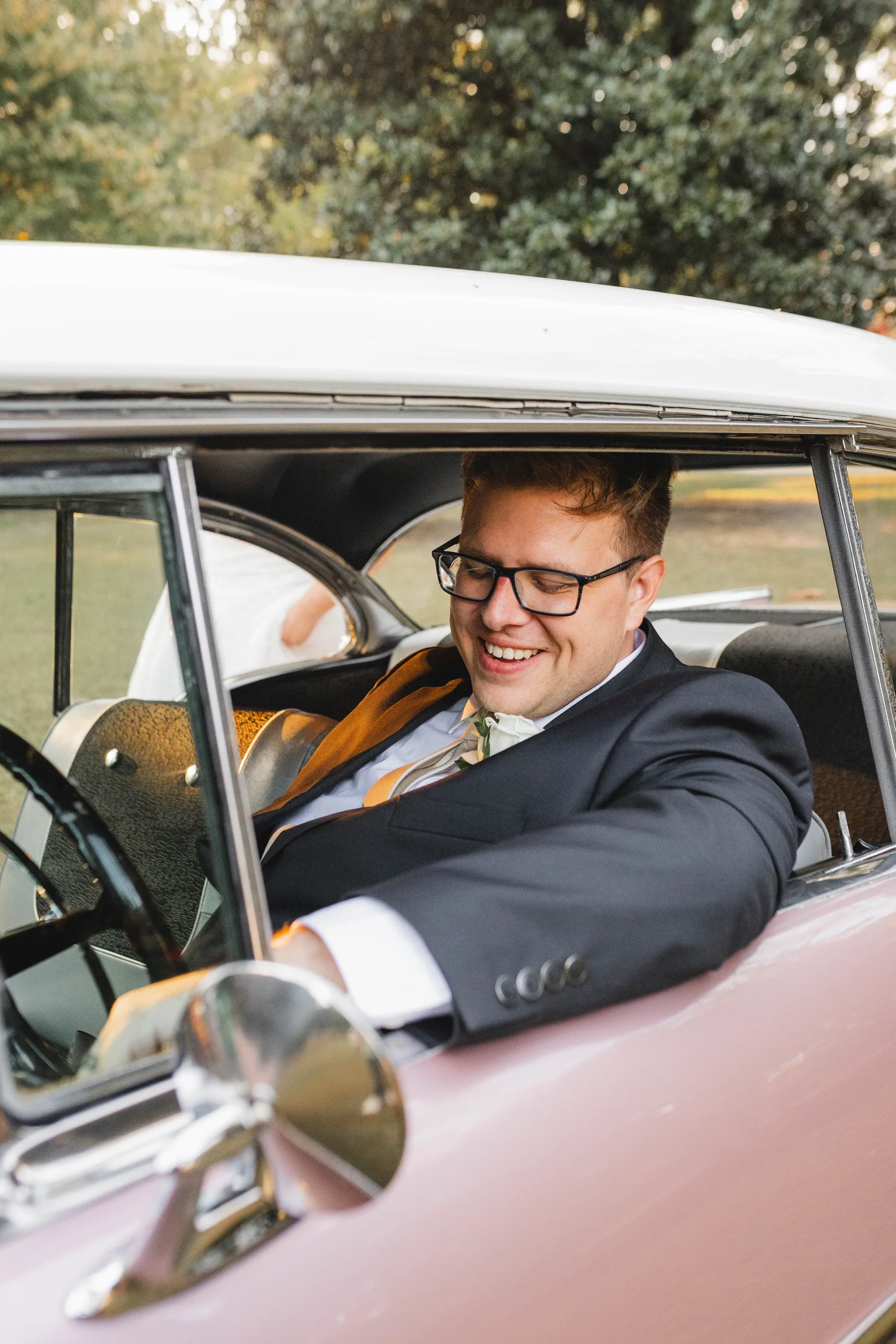 Wedding Formals: the groom laughing behind the wheel of the pink Chevrolet, at their wedding at Naylor Hall in Roswell, GA