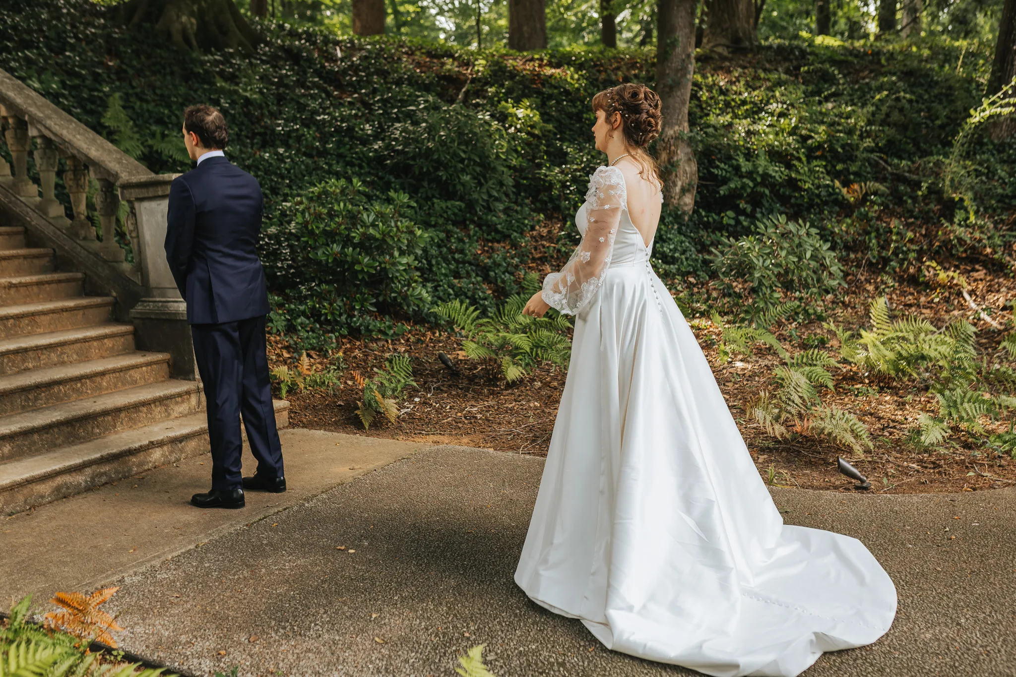 First Look: the bride walking up behind the groom by the stone steps, on their wedding day at Cator Woolford Gardens in Atlanta, GA