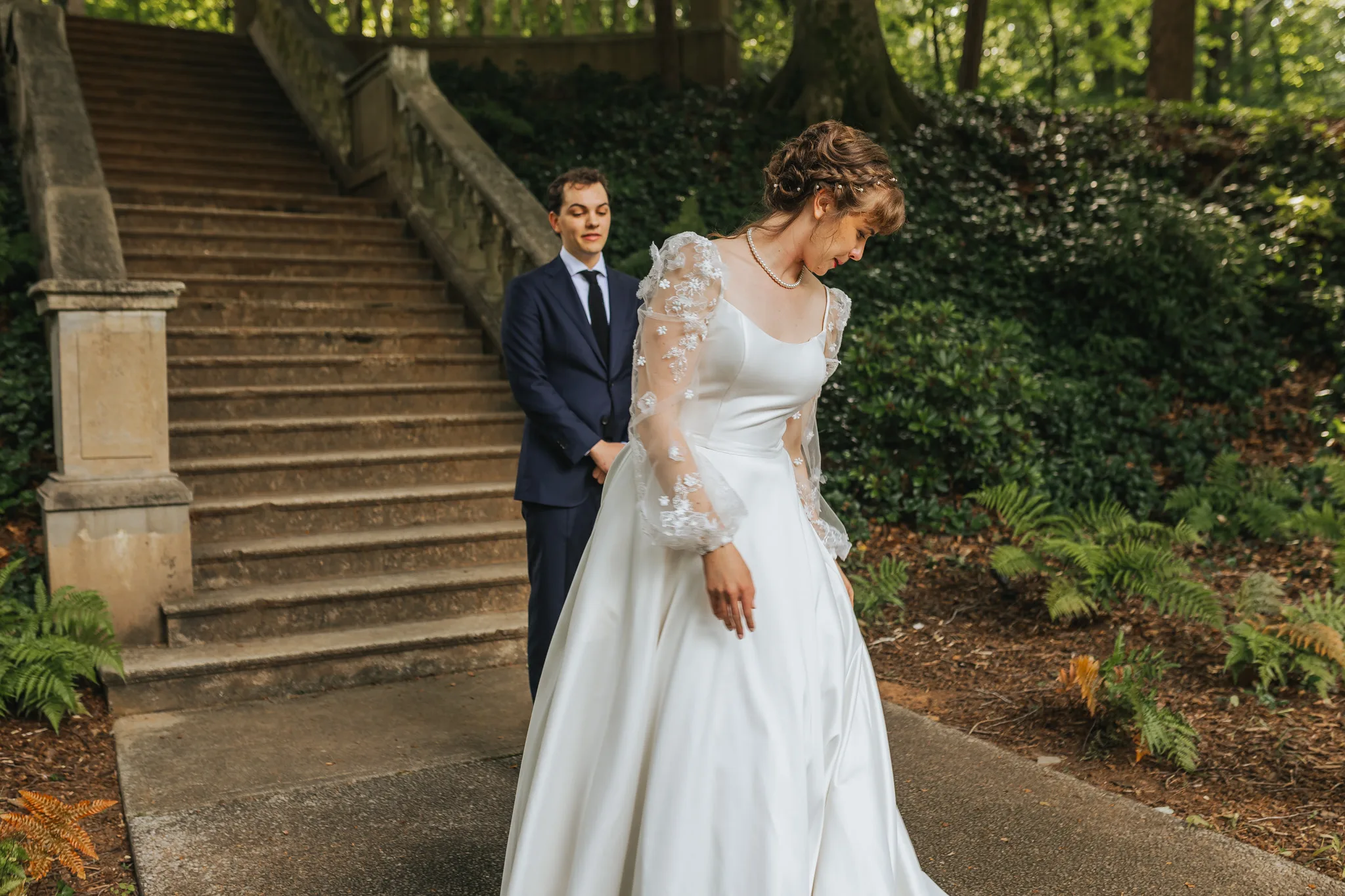 Bridal Portraits: the bride in her lace sleeves with the groom waiting on the staircase, on their wedding day at Cator Woolford Gardens in Atlanta, GA