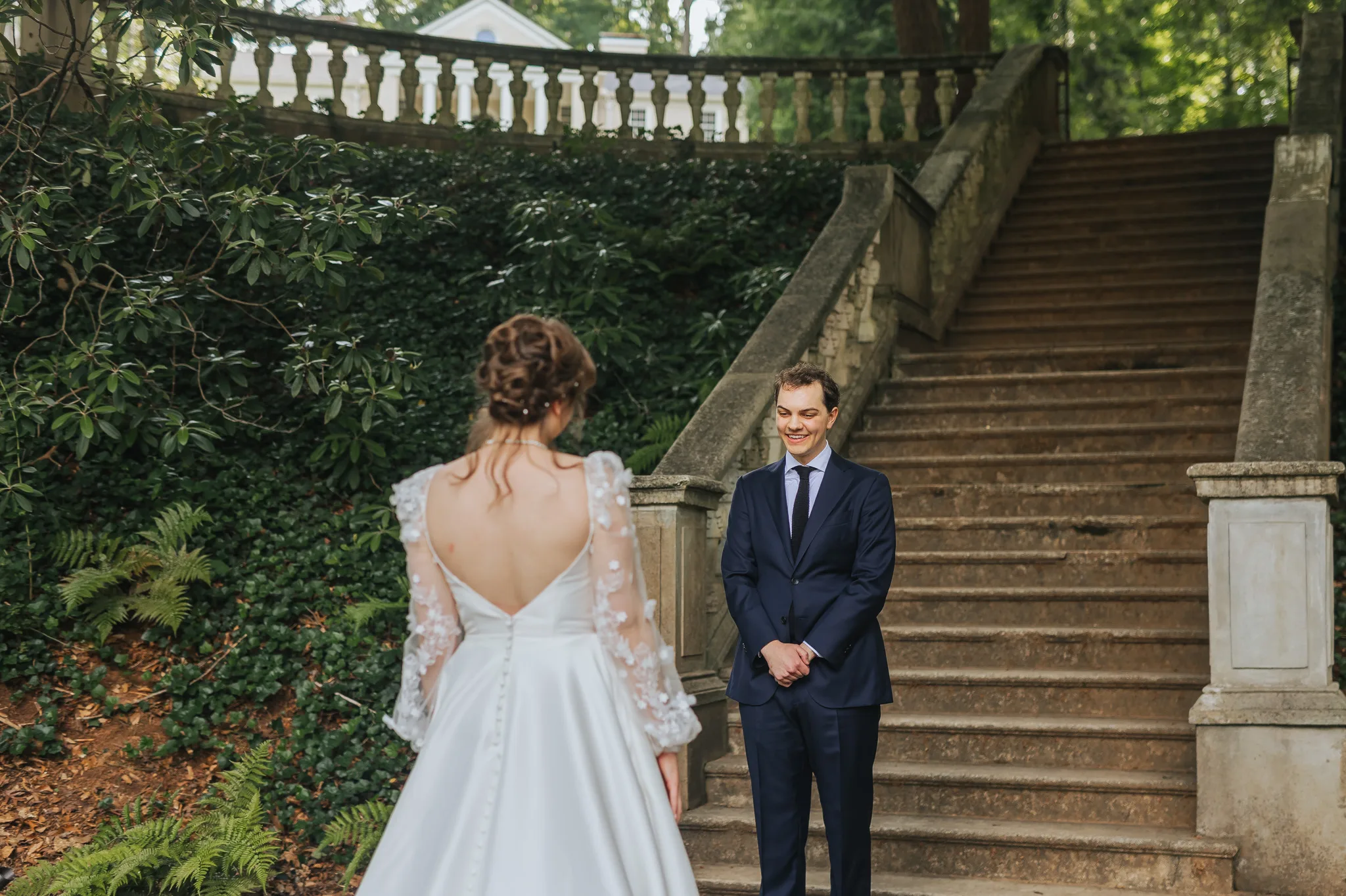 First Look: the bride walking toward the groom at the foot of the stone staircase, on their wedding day at Cator Woolford Gardens in Atlanta, GA