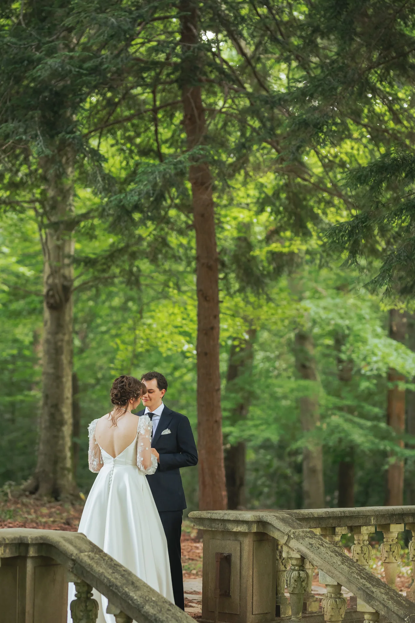 Wedding Formals: an embrace by the stone balustrade in the woods, on their wedding day at Cator Woolford Gardens in Atlanta, GA