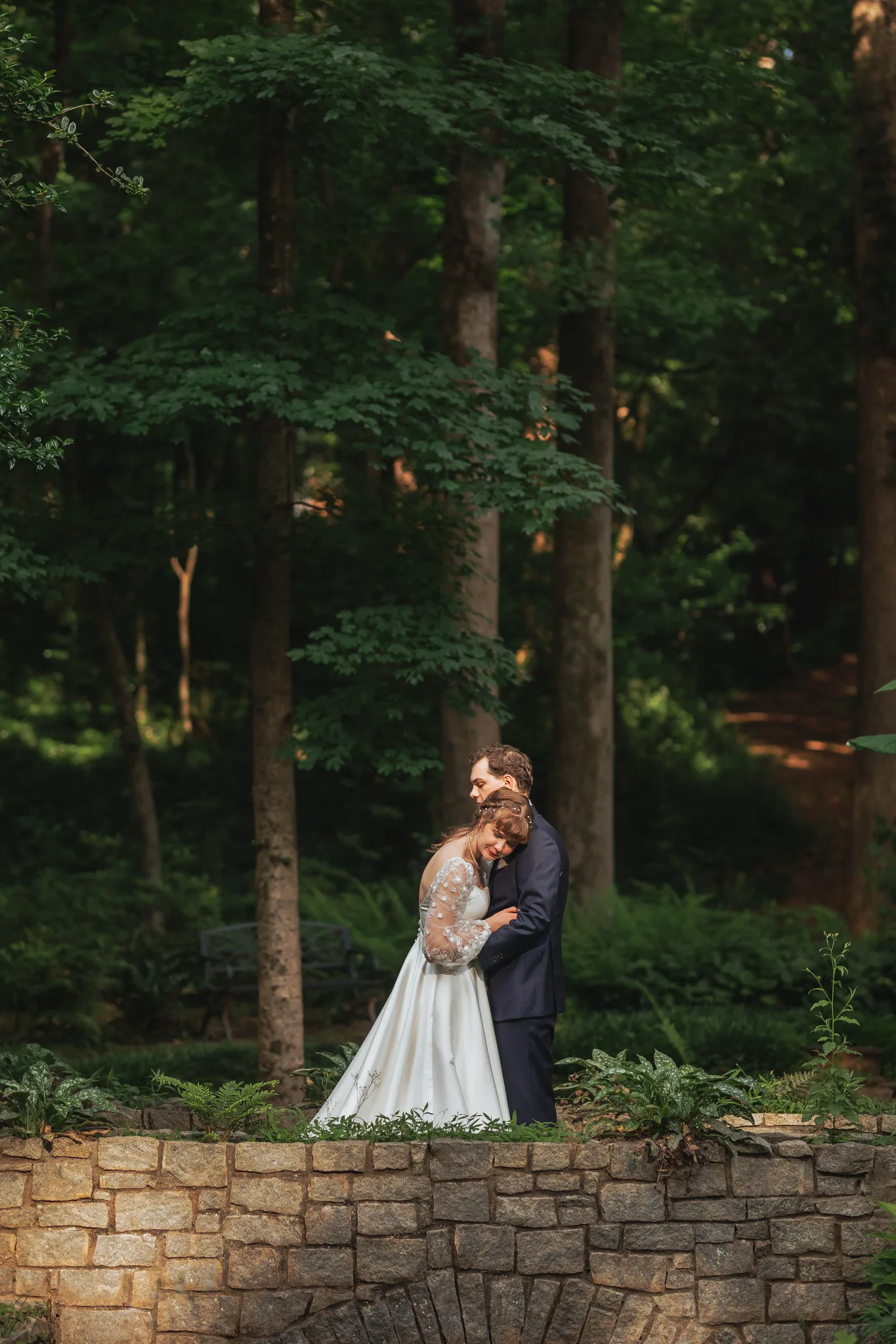 Wedding Formals: a hug on the stone bridge with ferns in front, on their wedding day at Cator Woolford Gardens in Atlanta, GA