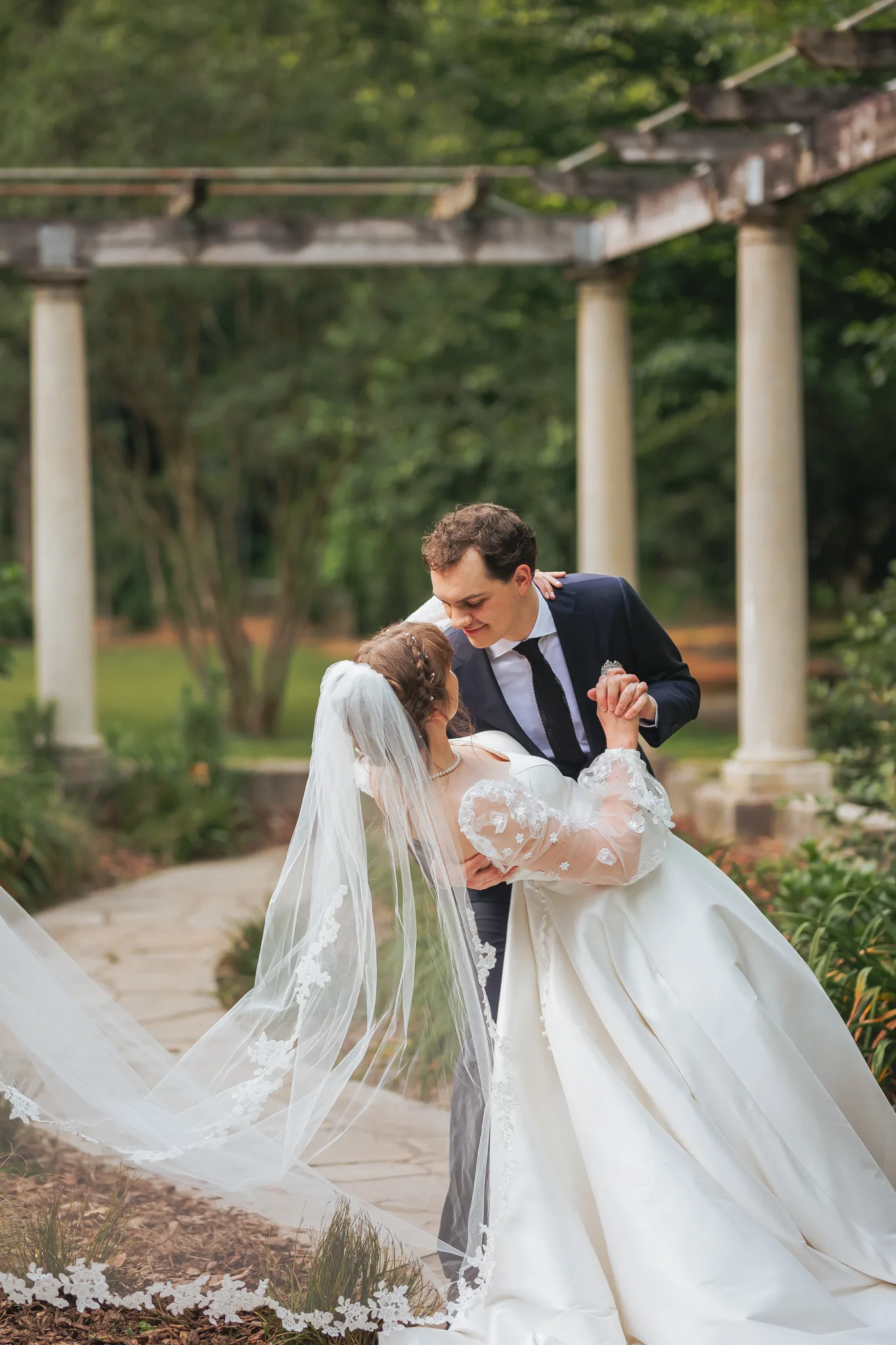 Wedding Formals: a dip kiss under the pergola, her veil in the air, on their wedding day at Cator Woolford Gardens in Atlanta, GA
