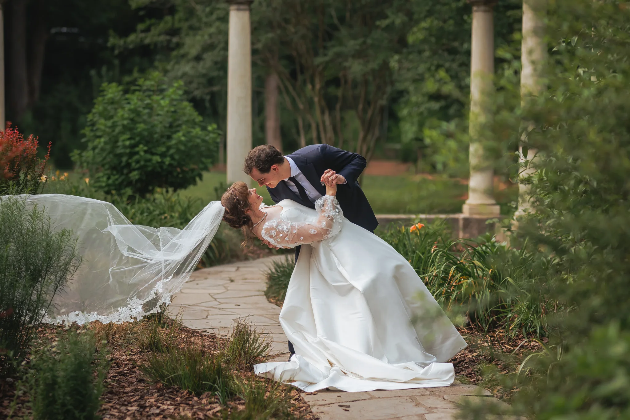 Wedding Formals: a dip kiss on the path, her veil flying, on their wedding day at Cator Woolford Gardens in Atlanta, GA