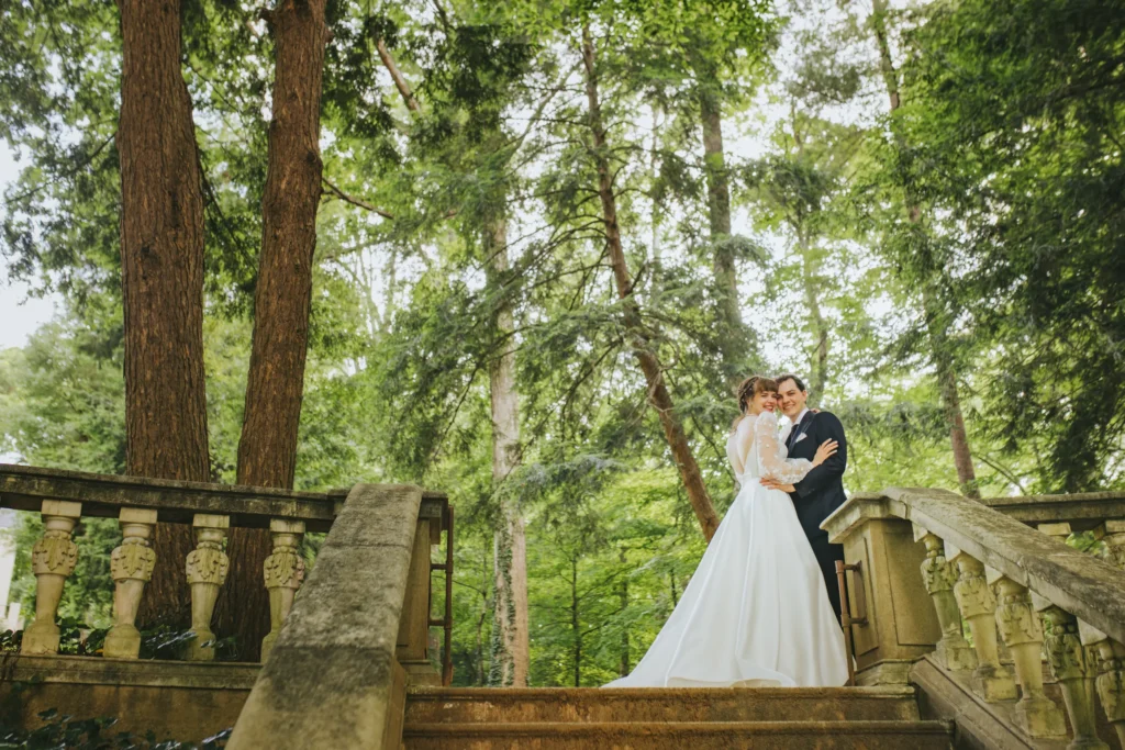Wedding Formals: embracing at the top of the stone steps under tall trees, on their wedding day at Cator Woolford Gardens in Atlanta, GA