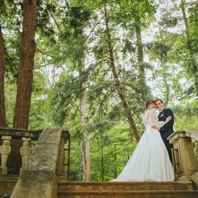 Wedding Formals: embracing at the top of the stone steps under tall trees, on their wedding day at Cator Woolford Gardens in Atlanta, GA