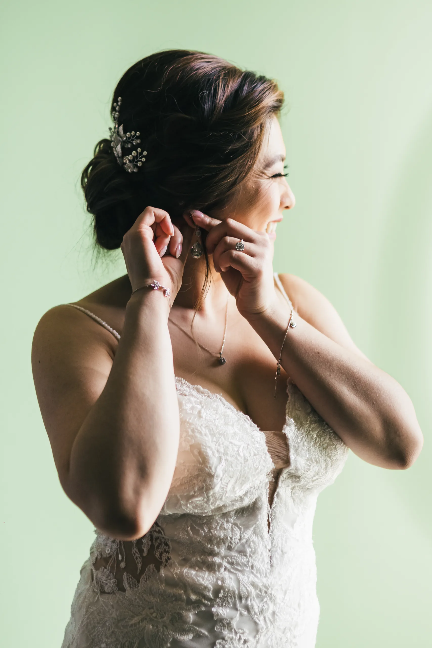 Getting Ready: the bride putting on her earrings against a green wall before their wedding at Holy Cross Catholic Church in Atlanta, GA