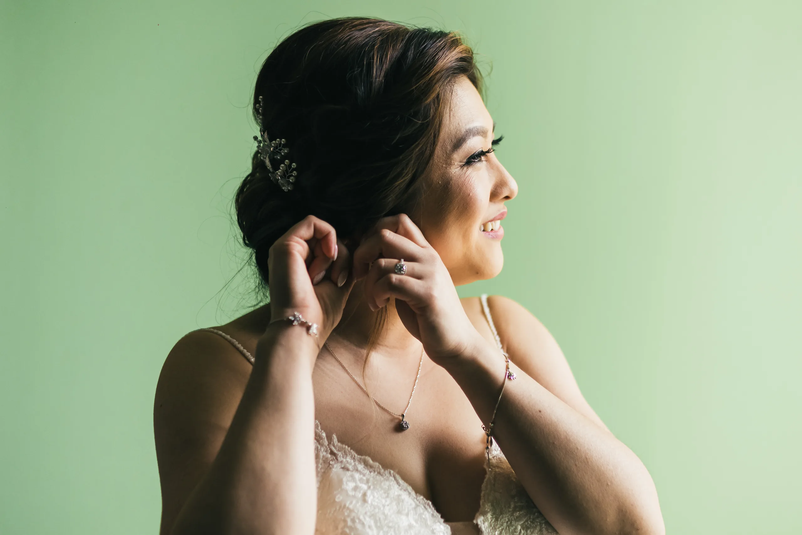 Getting Ready: the bride smiling as she puts on her earrings before their wedding at Holy Cross Catholic Church in Atlanta, GA